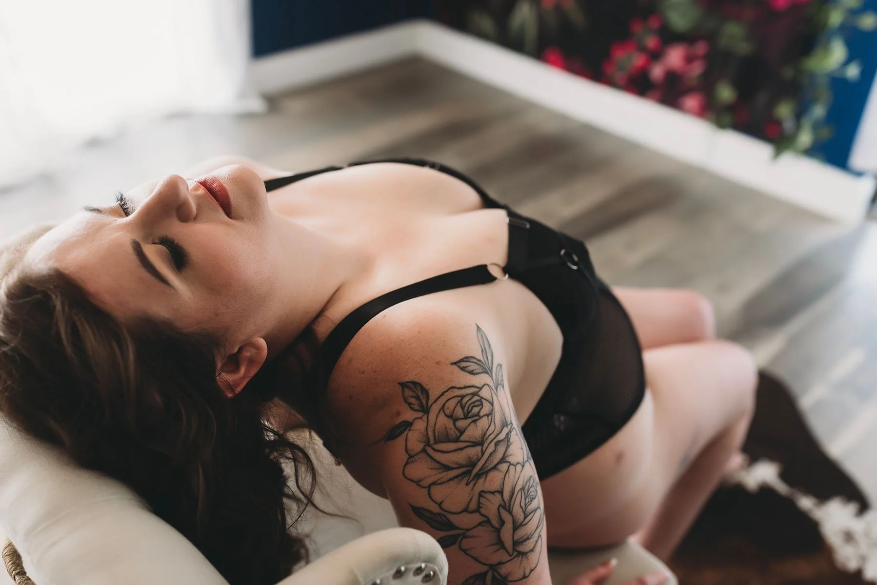 Tattooed woman in black lingerie arching back over a white chair in a Tampa boudoir studio