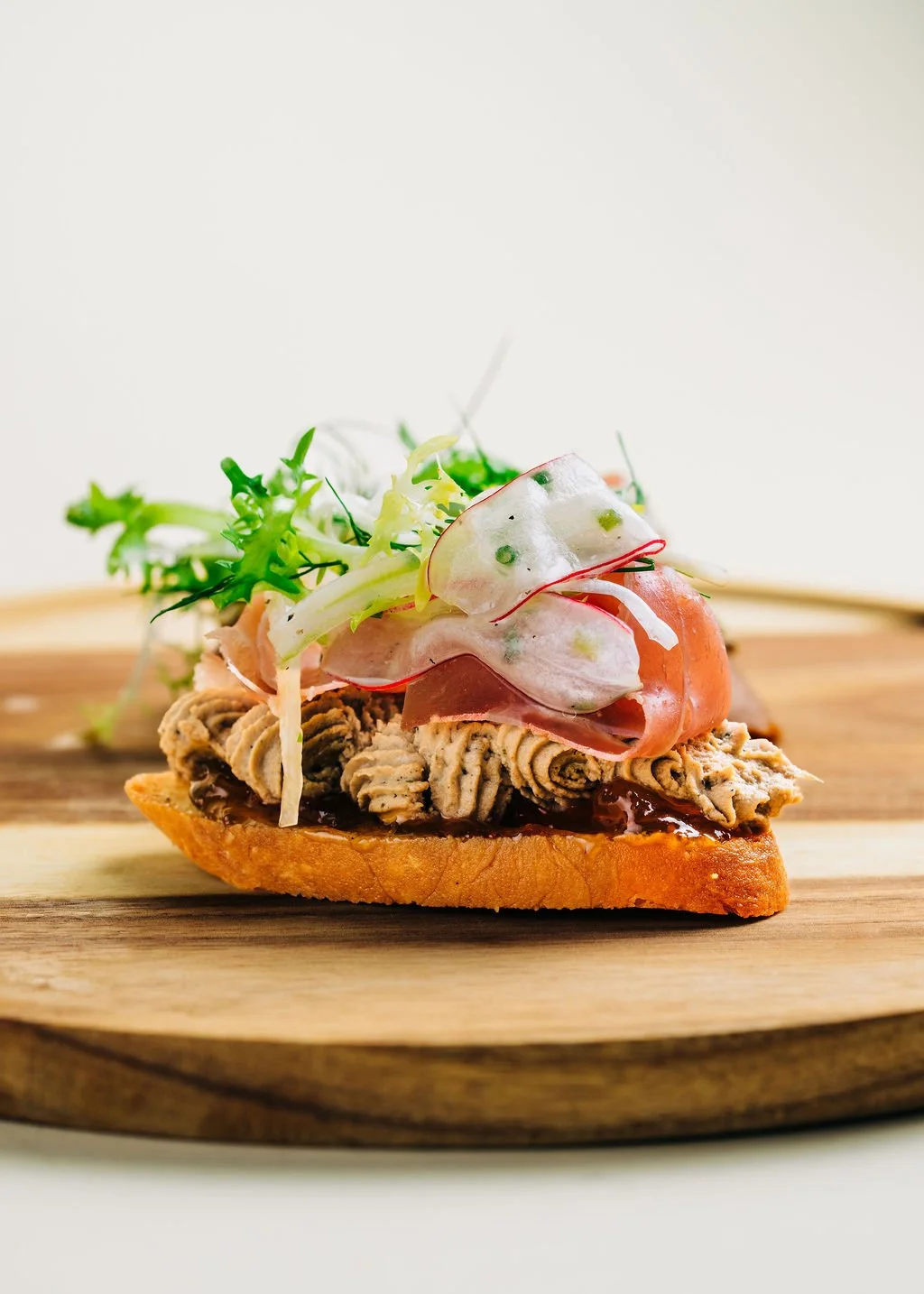 Open-faced sandwich with a thick slice of toasted bread topped with pasta salad, sliced turkey, and fresh greens, on a wooden serving board.