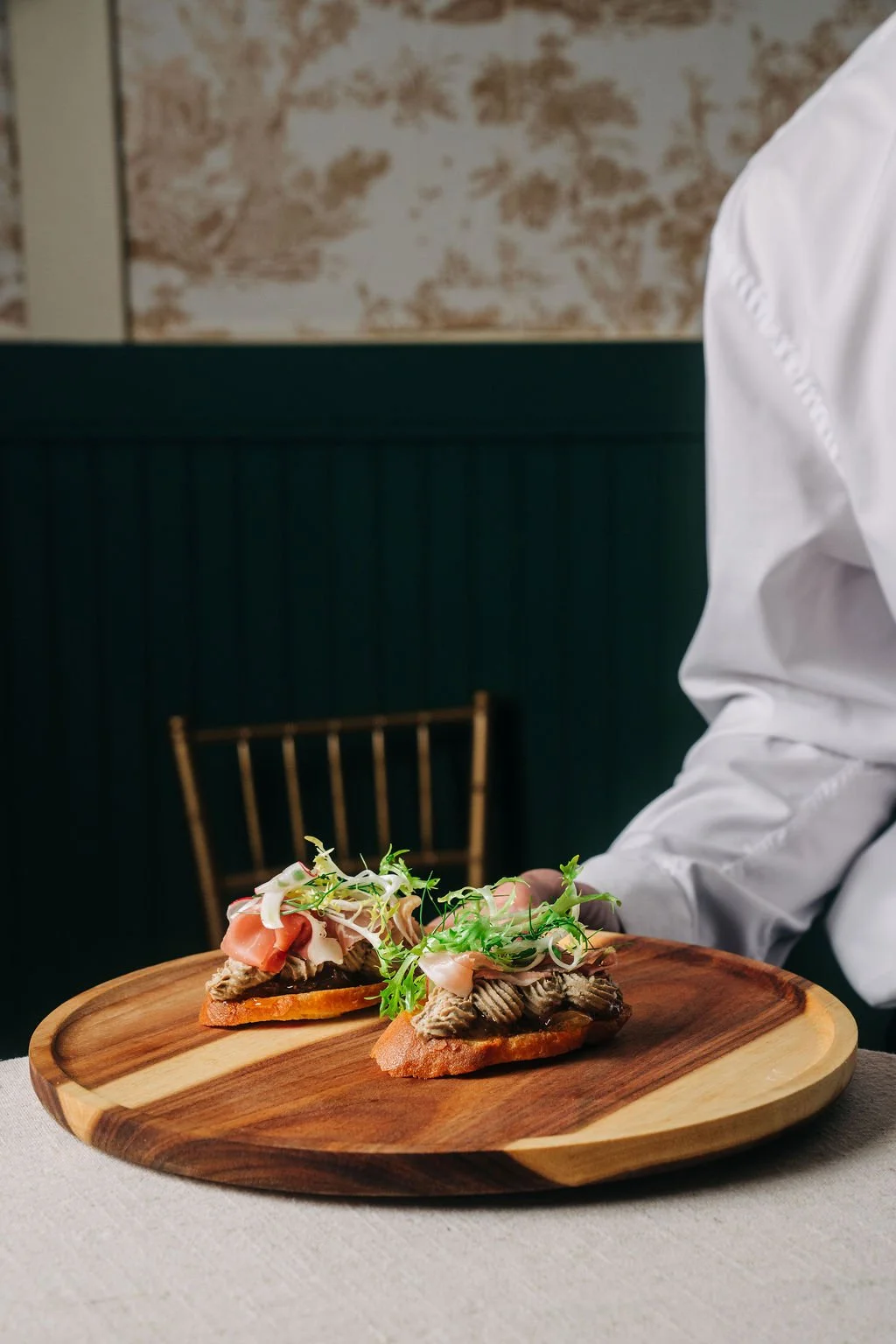 Two open-faced sandwiches topped with meat, cheese, and microgreens on a wooden platter.