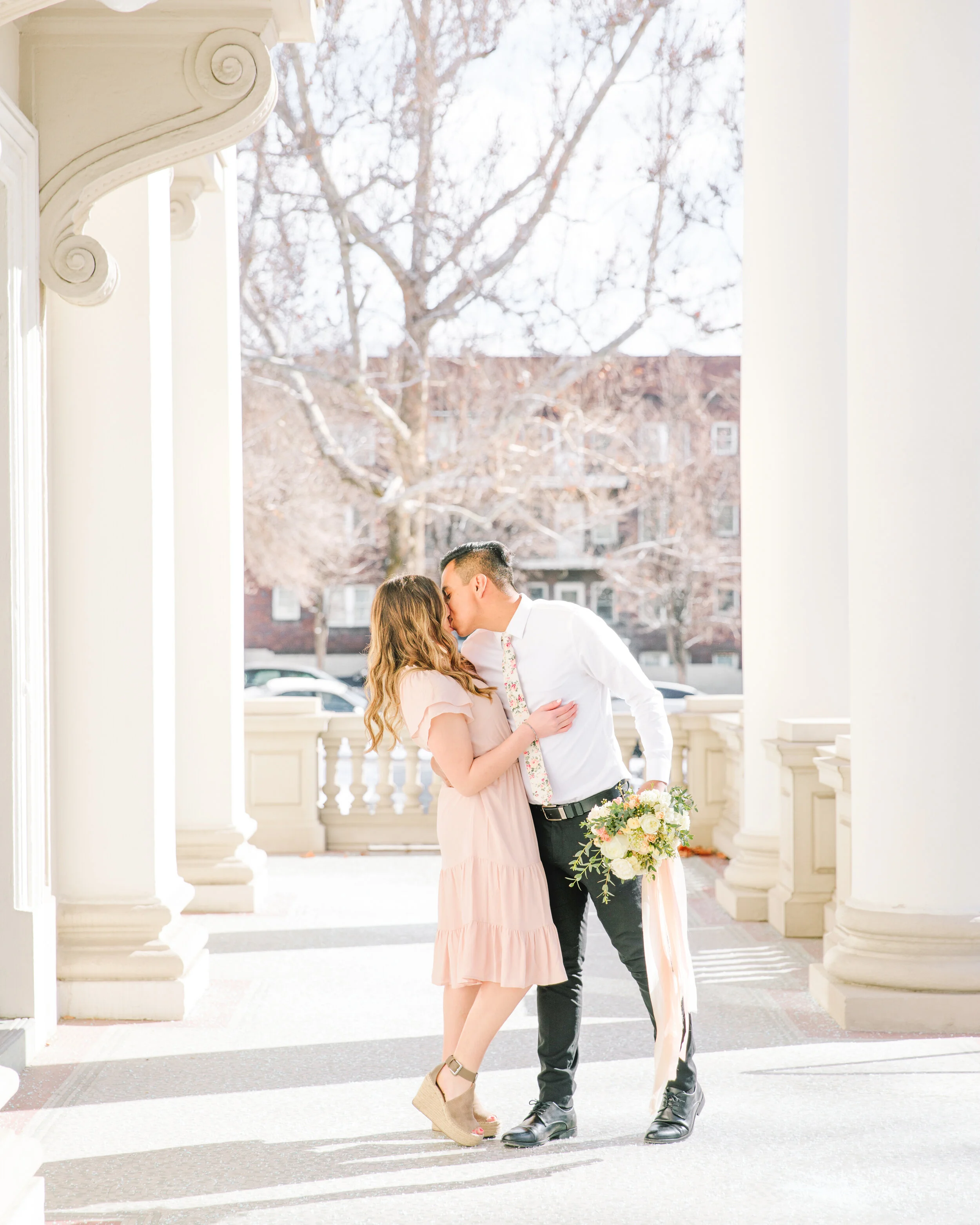  pose with the bouquet soon to be man and wife pose inspiration kissing pose inspiration mens outfit inspiration soft pink short sleeve flowing dress soft colors and bright lighting beautiful location couple kissing goals romantic kissing pose inspir