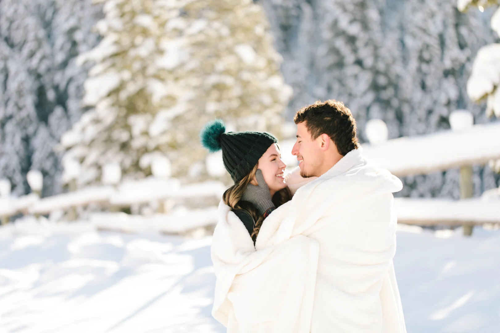  wrapped in a white blanket photo shoot ideas photo shoot in the snow winter photo shoot outfit inspiration cute black and blue beanie bright white snow winter engagement session ideas and inspiration all in white semi formal winter engagement photo 