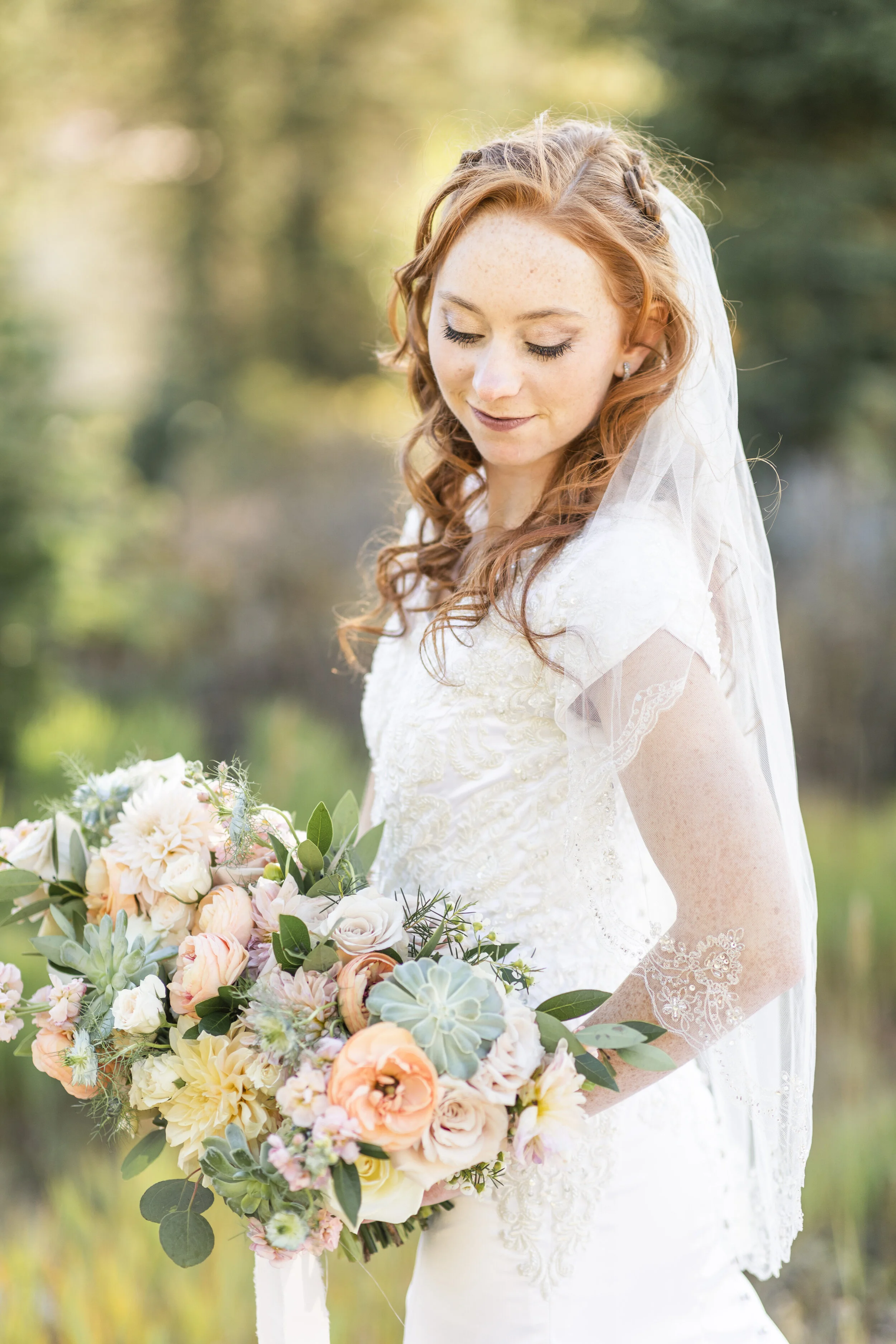  Stunning bride looking down at her budding bouquet natural wedding make up subtle bride make up blush bouquet greenery classic veil bride pose inspiration classic bridals modest wedding gown lds wedding inspo loose curls bride hairstyle ideas short 