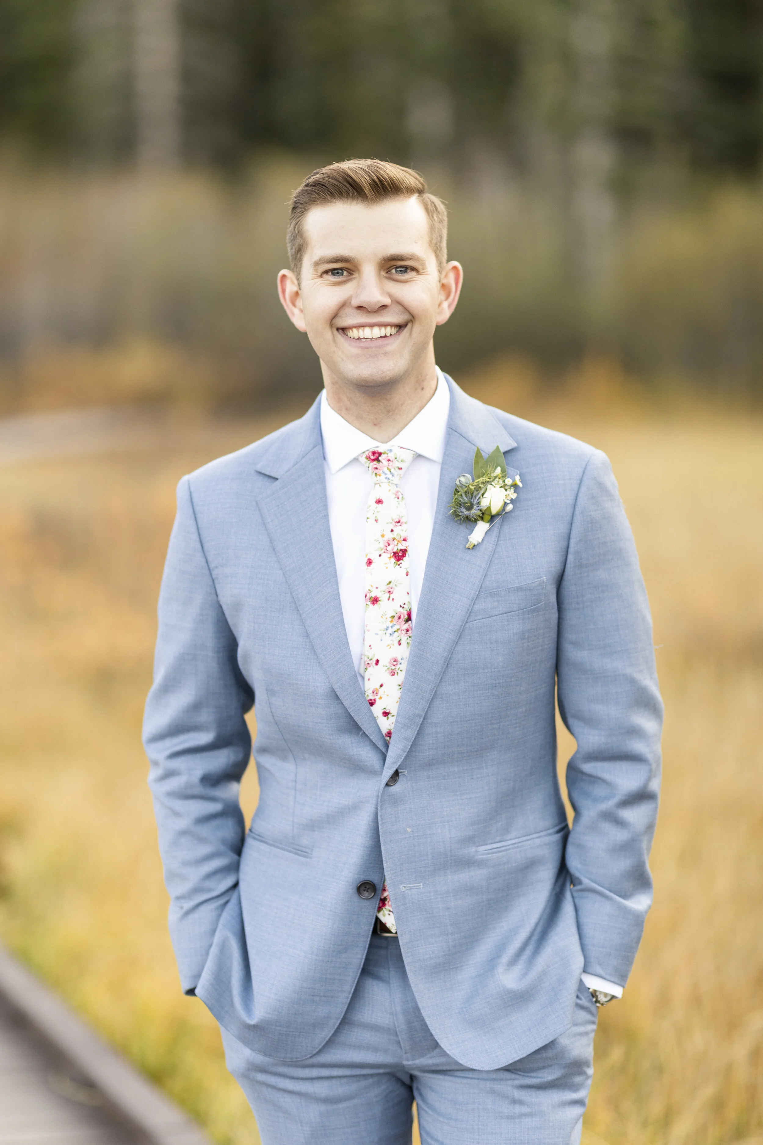  Handsome groom in white floral tie red floral tie groom hairstyle ideas mens haircut ideas green boutonniere steel blue gray suit groom portrait groom pose inspo blurred background true to color editing professional wedding portrait groomsmen outfit
