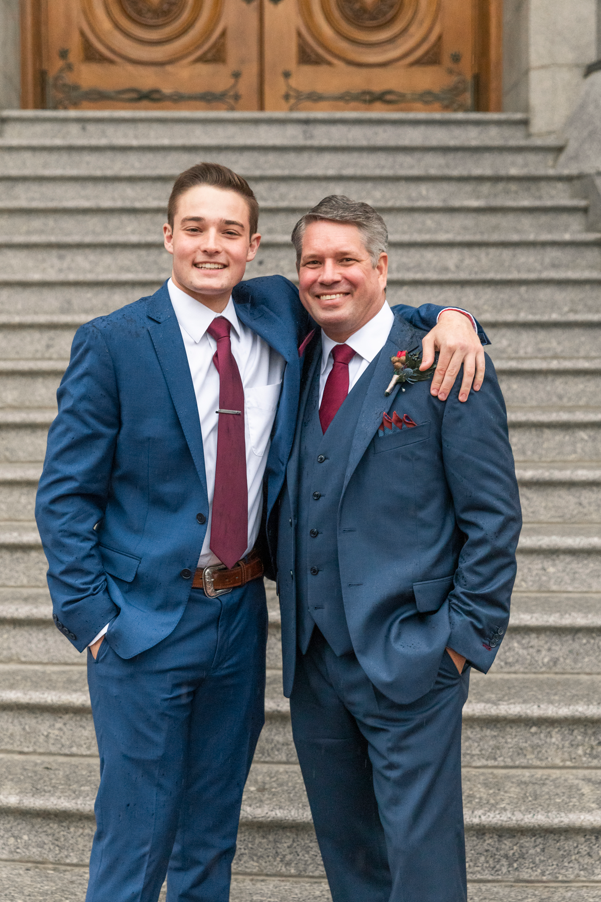  father son wedding photos navy wedding suits cranberry red wedding tie red boutonniere staircase salt lake city lds temple rainy wedding day happy hugging professional salt lake city wedding photographer #saltlakeldstemple #saltlakecityutah #temples
