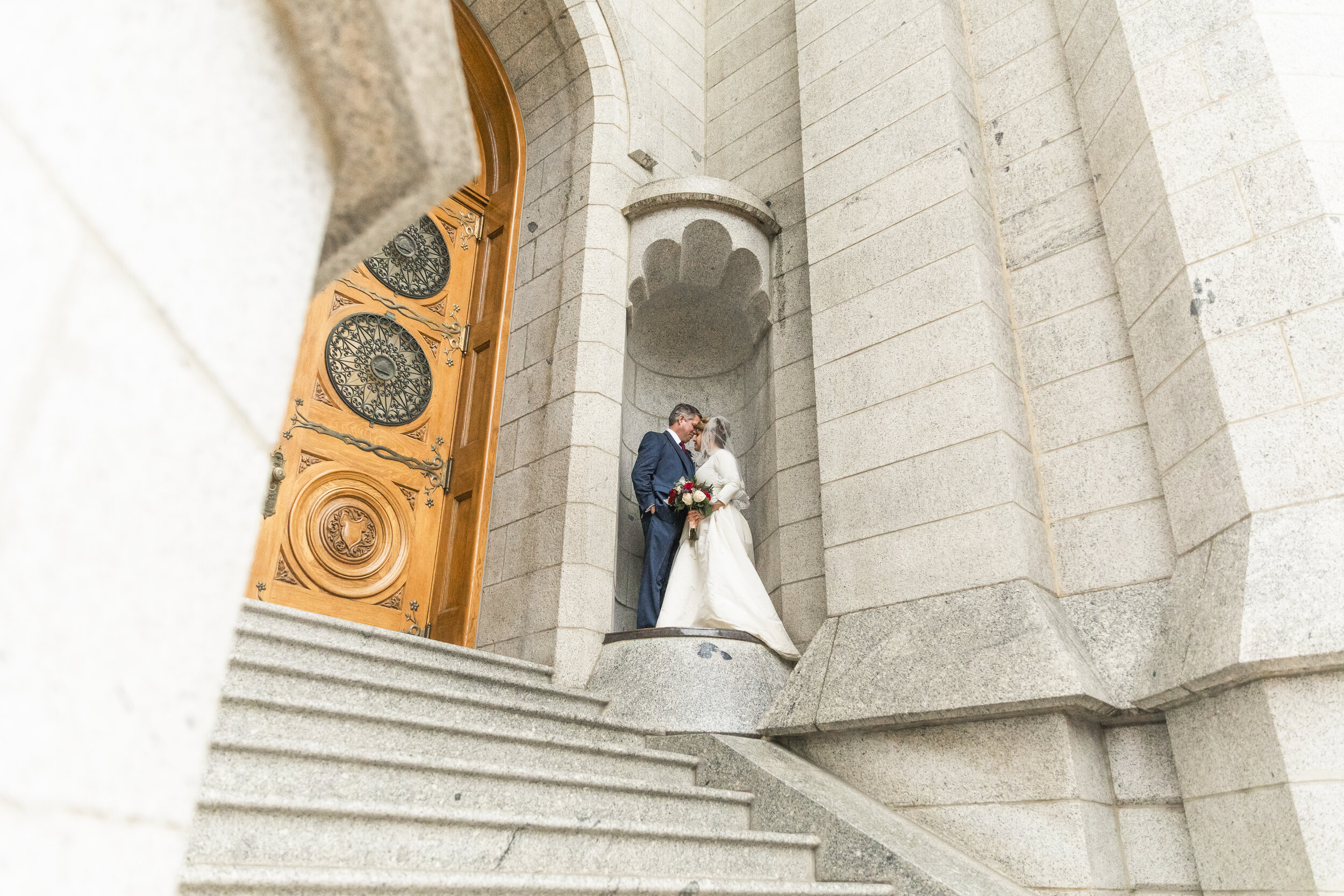  salt lake city lds temple stairs tall wooden doors pedestal wedding photos bride and groom hugging kissing happy just married temple square rainy wedding day professional utah valley wedding photography #saltlakeldstemple #saltlakecityutah #templesq