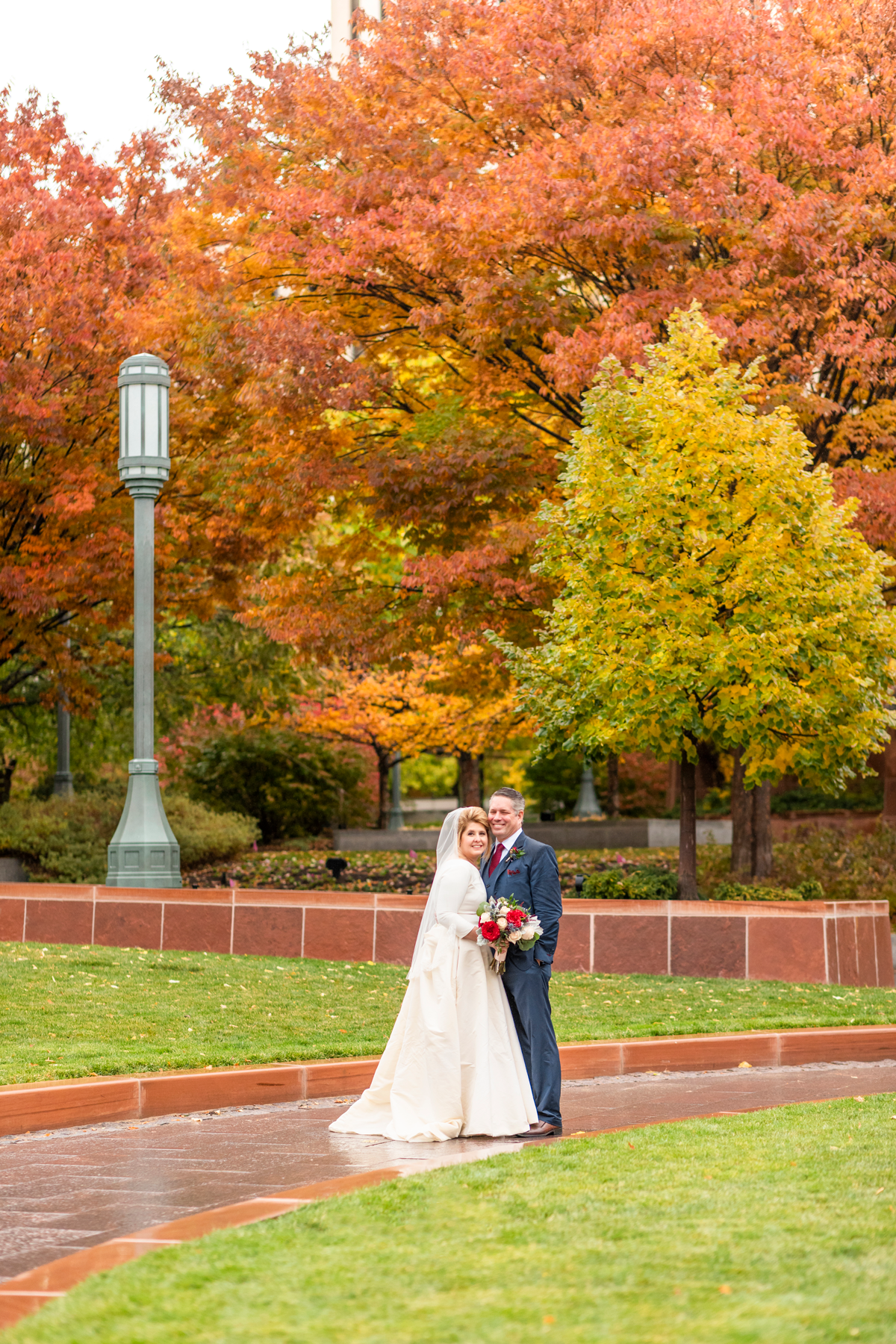  red orange green fall colored leaves salt lake city lds temple grounds just married hugging smiling rainy wedding day fall wedding red and white rose wedding bouquet professional salt lake city wedding photographer #saltlakeldstemple #saltlakecityut
