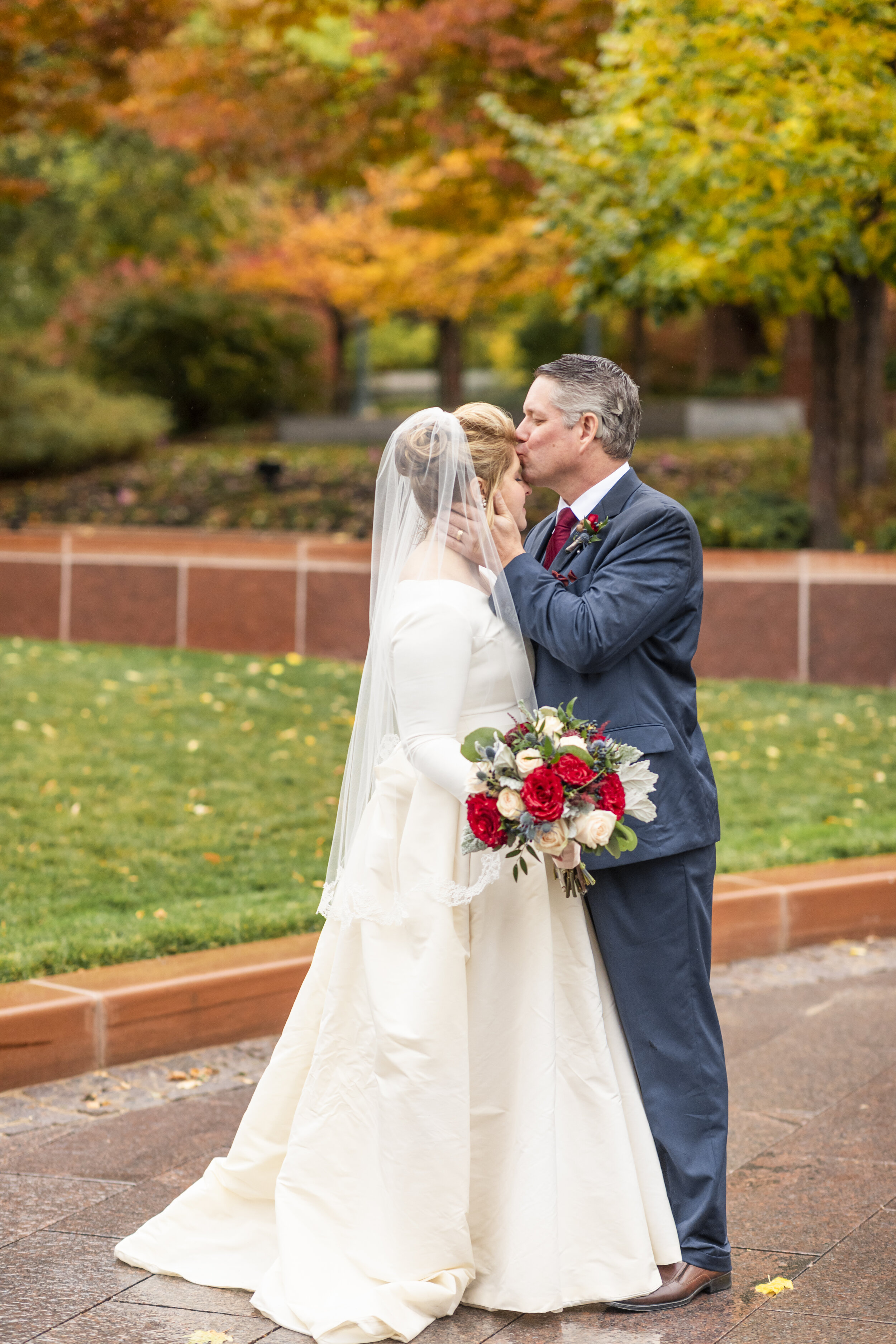  temple square grounds just married lds sealed romantic hugging kissing forehead modest long sleeved ballgown dress three quarter length wedding veil red and white rose wedding bouquet professional utah valley wedding photographer #saltlakeldstemple 