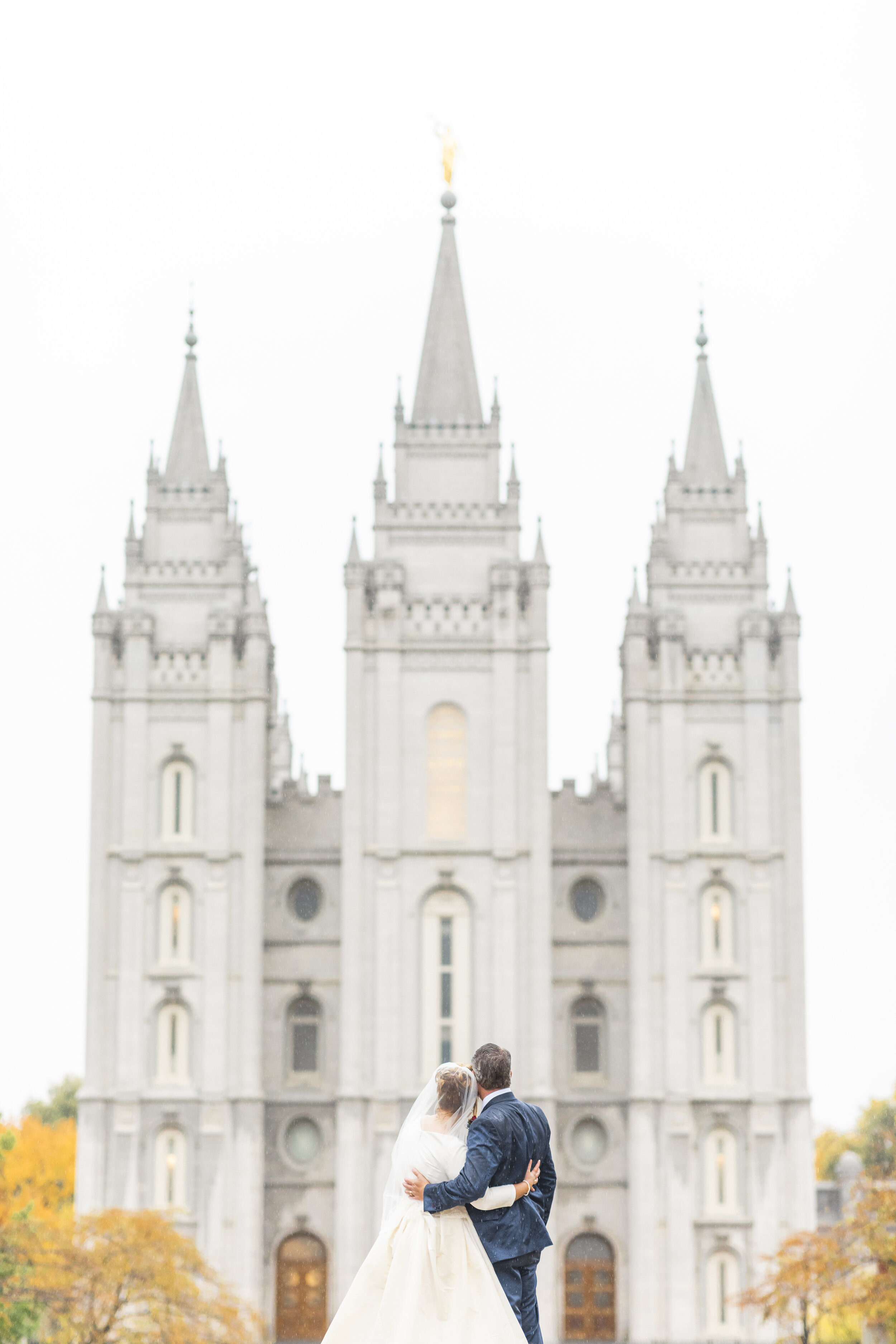  salt lake lds temple skyline yellow leaves rainy fall wedding day bride and groom hugging eyes to the temple just married temple square professional utah valley wedding photographer #saltlakeldstemple #saltlakecityutah #templesquare #sealing #justma