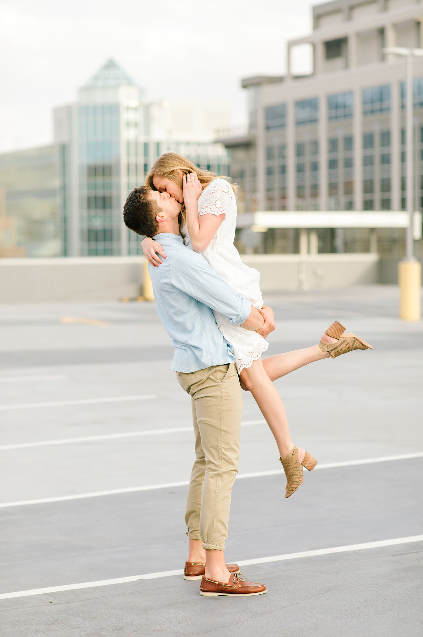  light blue collared casual shirt white lace short sleeve dress loose hanging curls lift toes pointed kissing photo engagement photo session rooftop photo shoot salt lake city utah professional utah valley engagement photographer #downtownsaltlakecit
