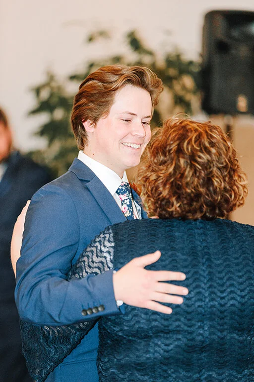        a happy groom smiling at his mother during their mother and son dance blue suit floral tie inspiration groom hairstyle inspiration curly hair mom first love mother of the groom wedding reception dancing family wedding loving memories wedding d