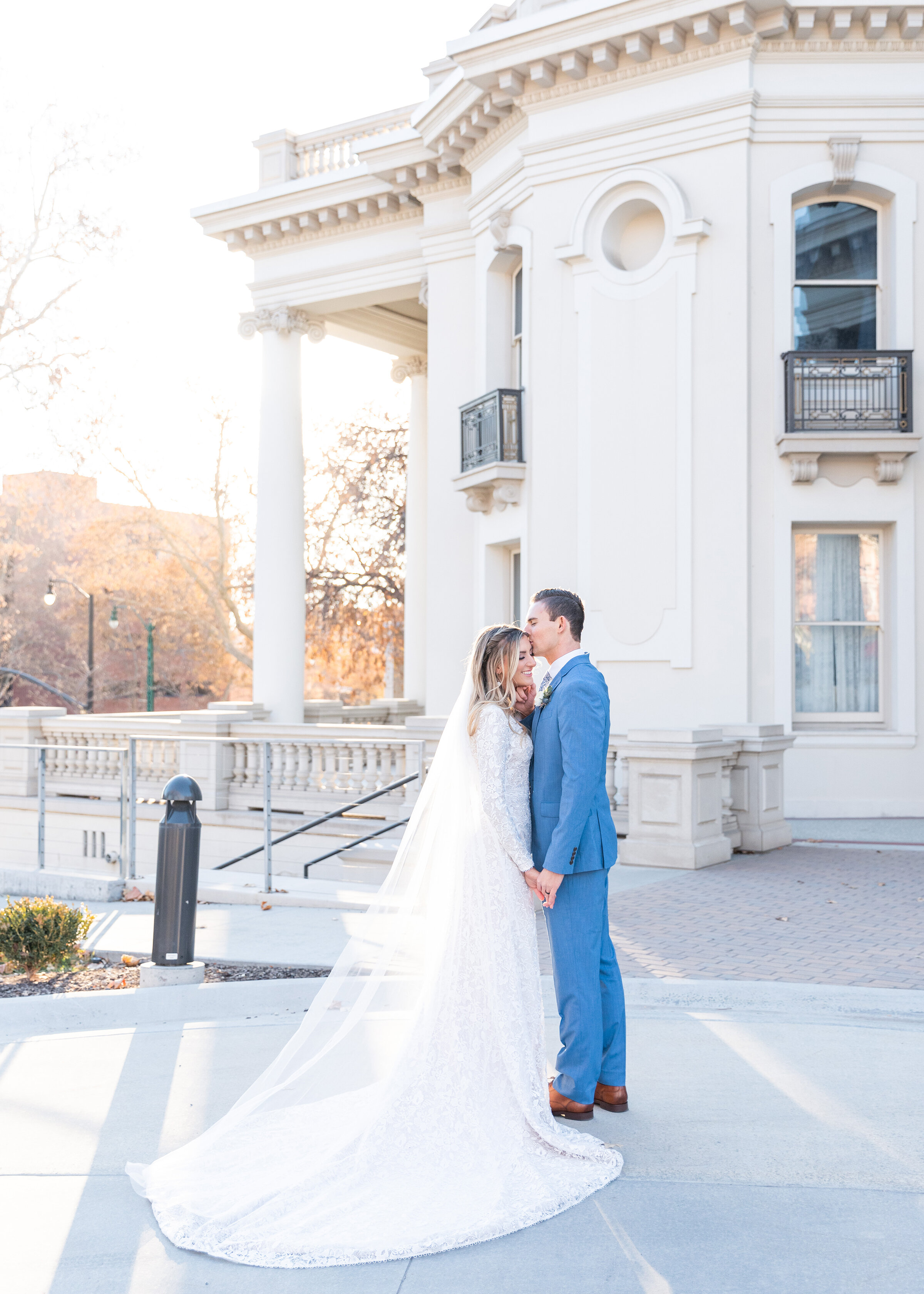  Clarity Lane Photography captures a romantic kiss shared between bride and groom outside their reception venue in Salt Lake County, Utah. professional salt lake county wedding photographer, wedding photo session, medium blue wedding suit, brown wedd
