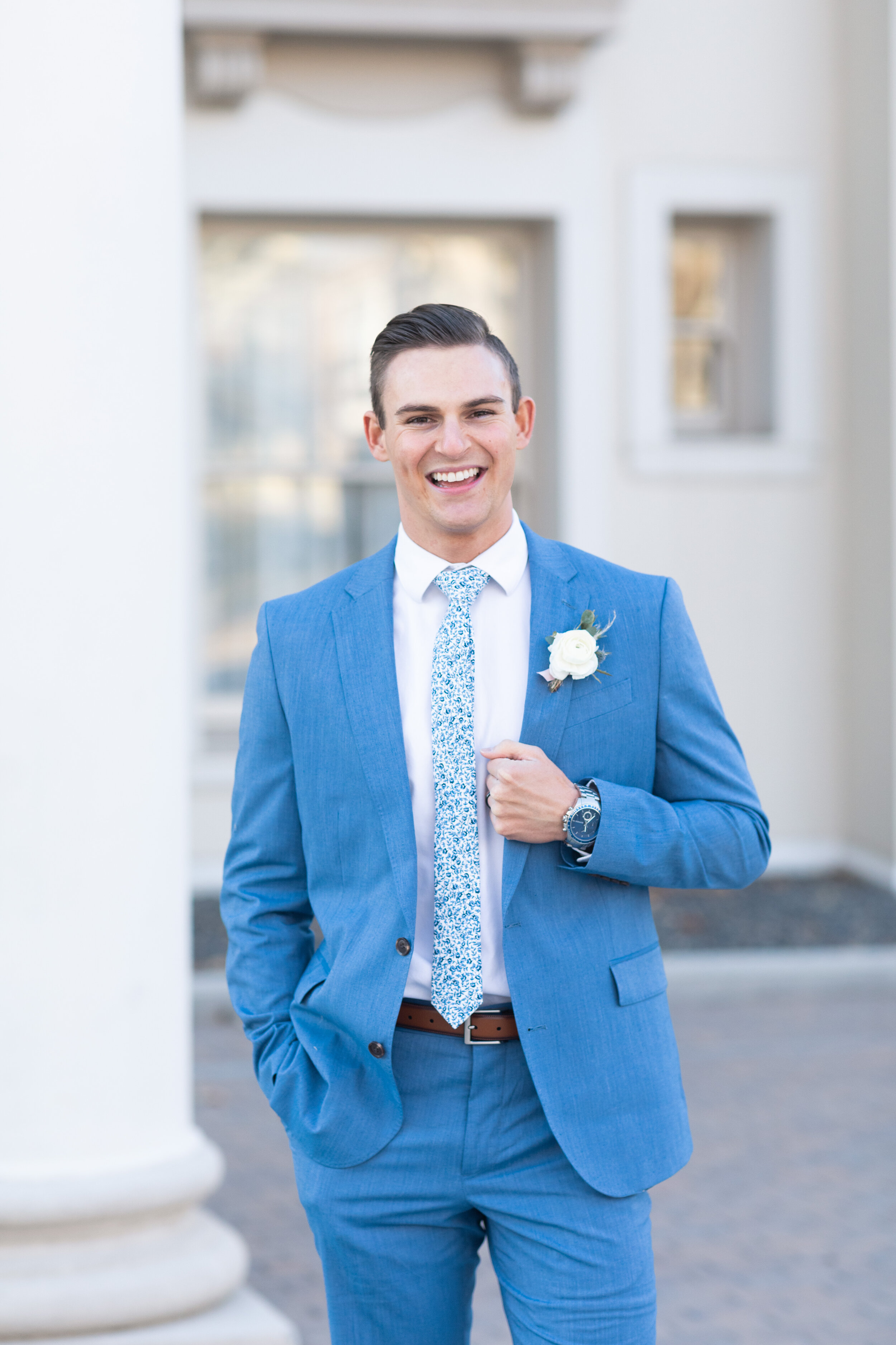  An eager groom poses for Clarity Lane Photography at his reception held at the Monson Center in Salt Lake City, Utah. bright blue wedding suit, groom hair inspiration, blue wedding colors, floral blue wedding tie, brown leather belt with blue suit, 