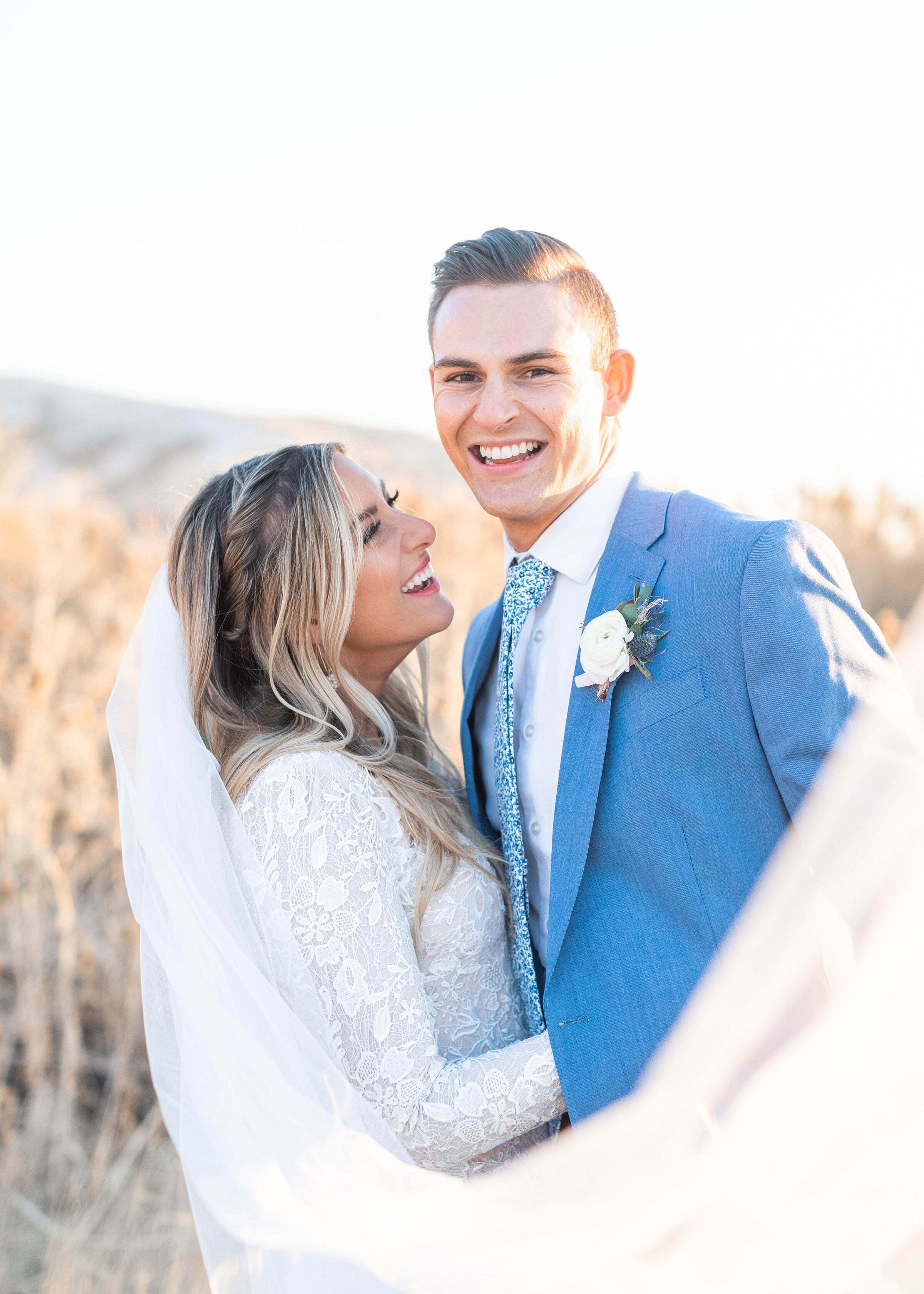  Surrounded by a field filled with tall grass, Clarity Lane Photography captures a bride and groom laughing together during their bridal session at Tunnel Springs Park in Salt Lake City, Utah. long billowy wedding veil, laughing bride and groom, brid