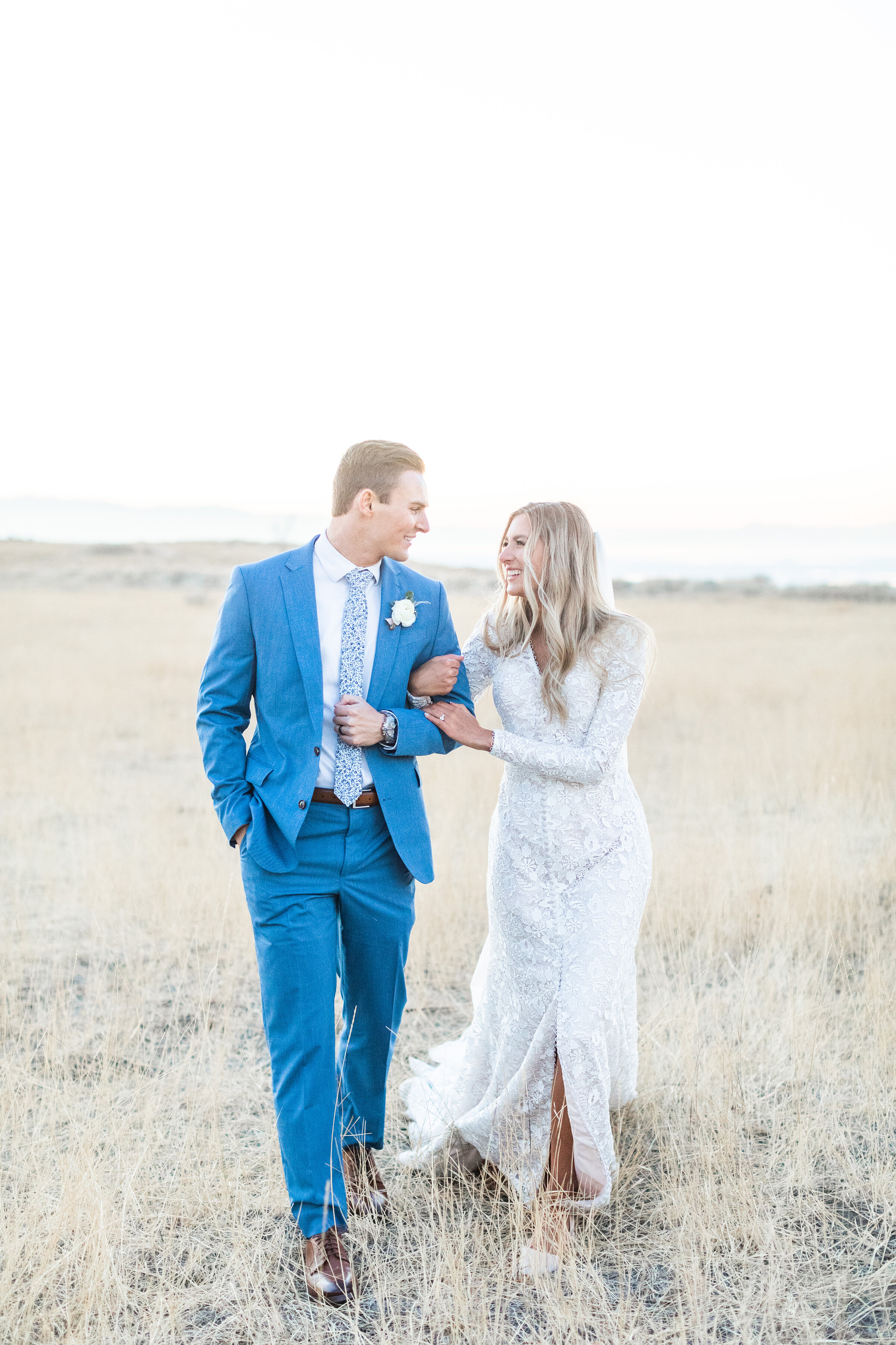  Clarity Lane Photography captures a Salt Lake City, Utah bride and groom walking with linked arms through and open grassy field. professional salt lake county wedding photographer, open grassy field bridal photos, clear skies wedding photos, medium 