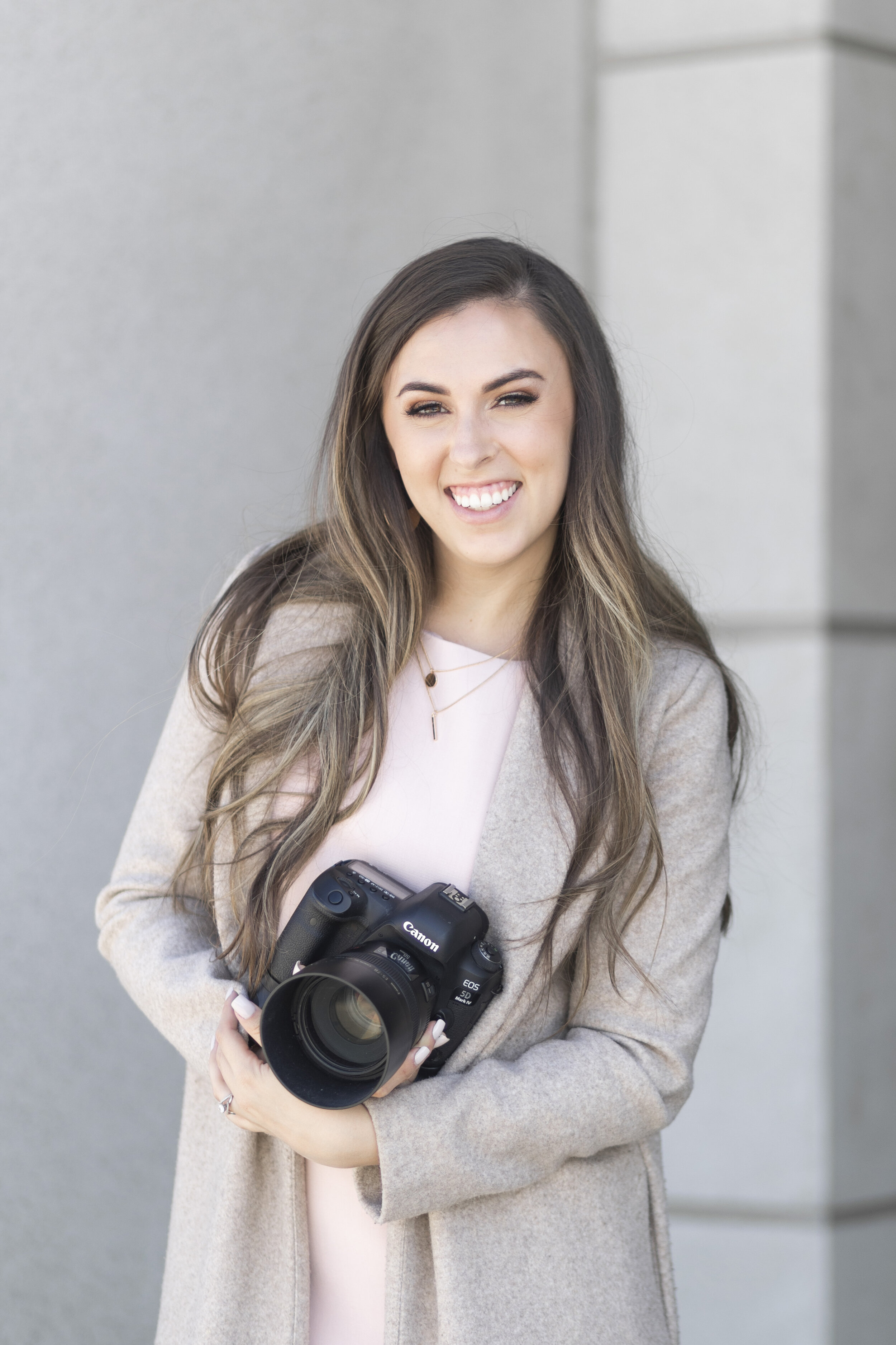  Posed with her Canon DSLR camera, professional photographer from Clarity Lane Photography poses for a brand photoshoot in Salt Lake, City, Utah. dslr camera, canon camera, khaki jacket, long balayage loose curled hair, brand photoshoot, professional