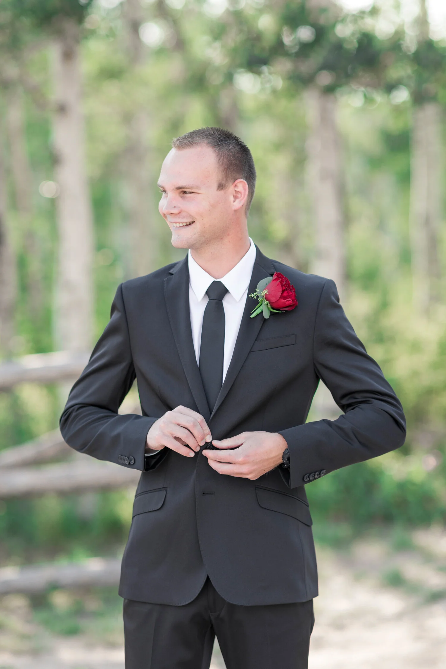  Groom buttoning his top button of his black suit, smiling in green lush mountains at Guardsman Pass in Park City, Utah captured by Clarity Lane Photography. groom photos groom formal photo red rose boutonniere guardsman pass photography groom style 