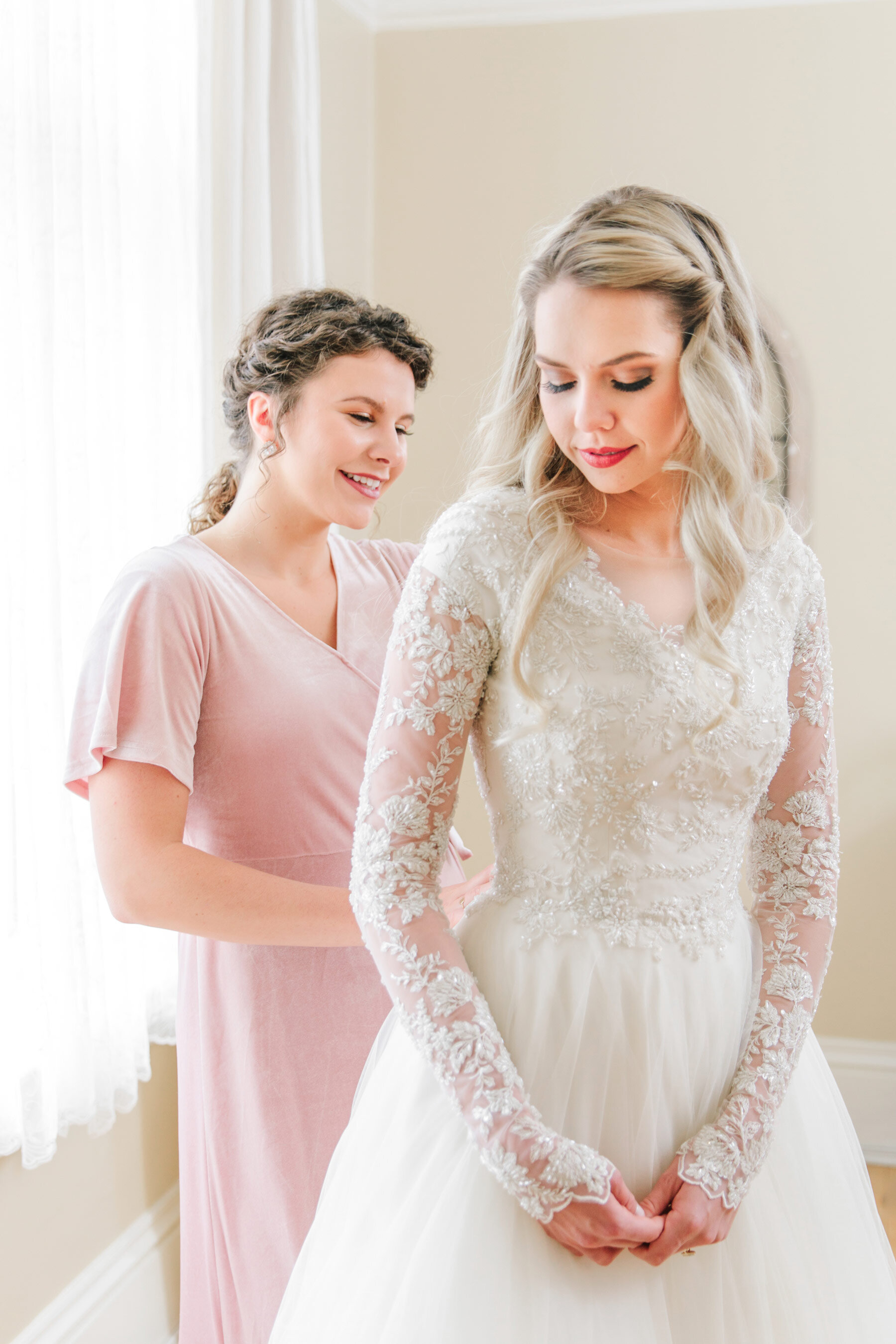  On her wedding morning,  wedding photographer, Clarity Lane captures this bridesmaid button up this bride's wedding dress. Salt Lake City wedding photographer lace long sleeve ivory modest wedding dress platinum blonde women's hair color light pink 