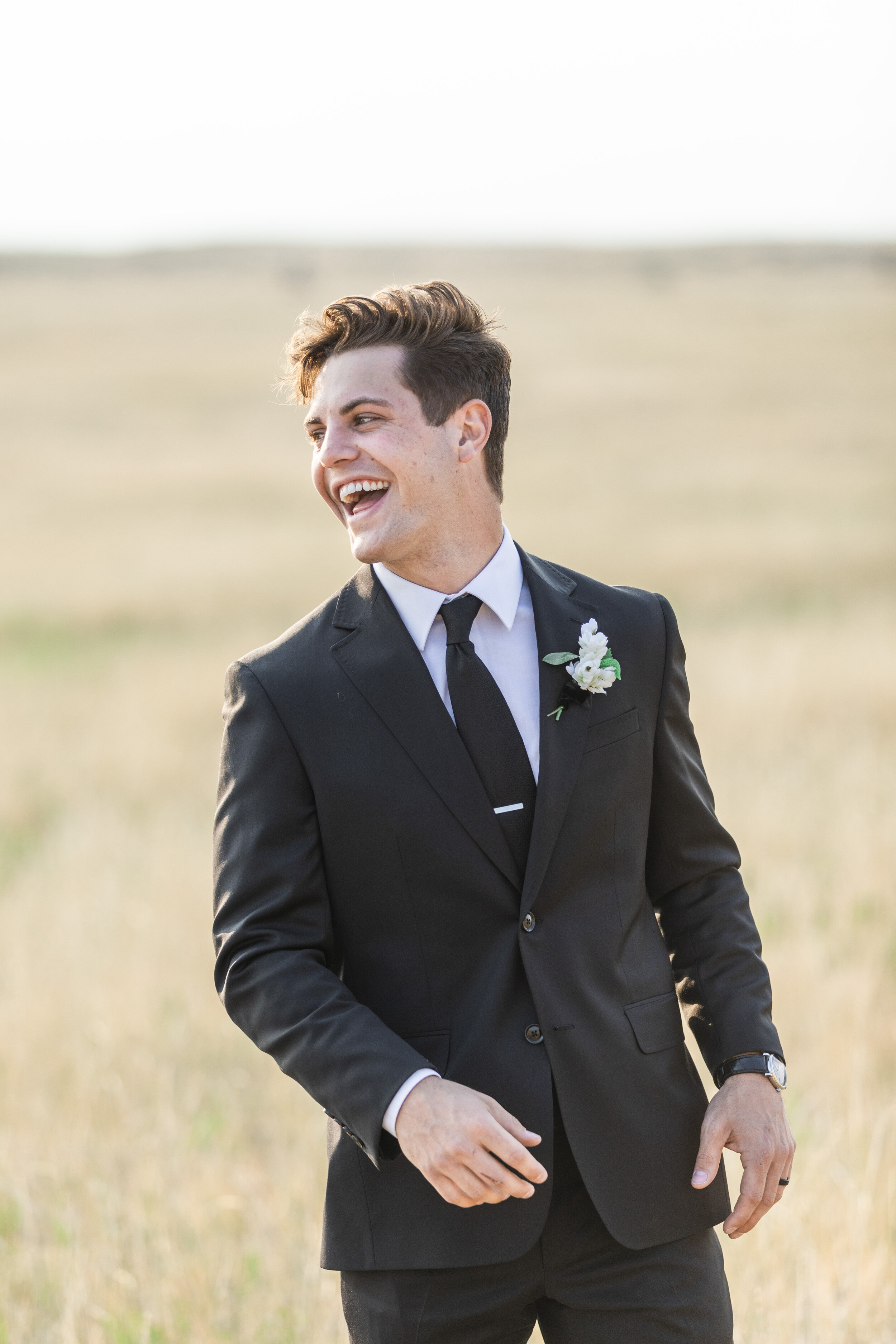  Groom wearing a black suit and black tie standing in a golden grass field at tunnel springs in Salt Lake County by Savanna Richardson Photography. tunnel springs wedding formals black suit on wedding happy groom #savannarichardsonphotography #savann