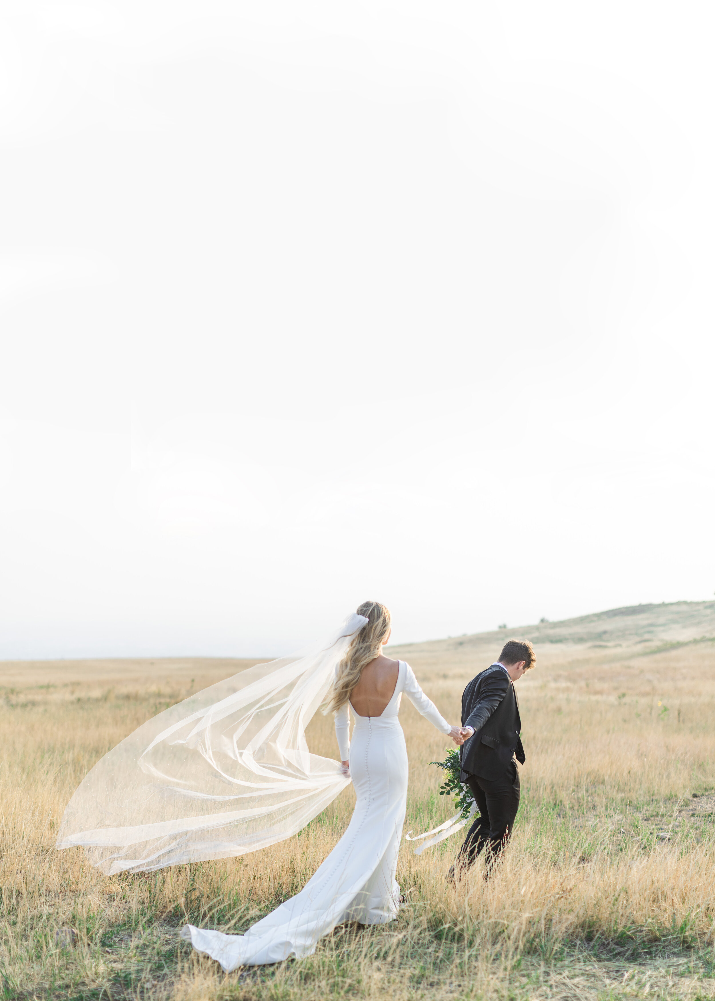  Savanna Richardson Photography captures a groom leading his bride by holding her hand in some golden rolling hills in Salt Lake City. long sleeve wedding gown big back dip wedding dress wedding veil blowing in wind #savannarichardsonphotography #sav