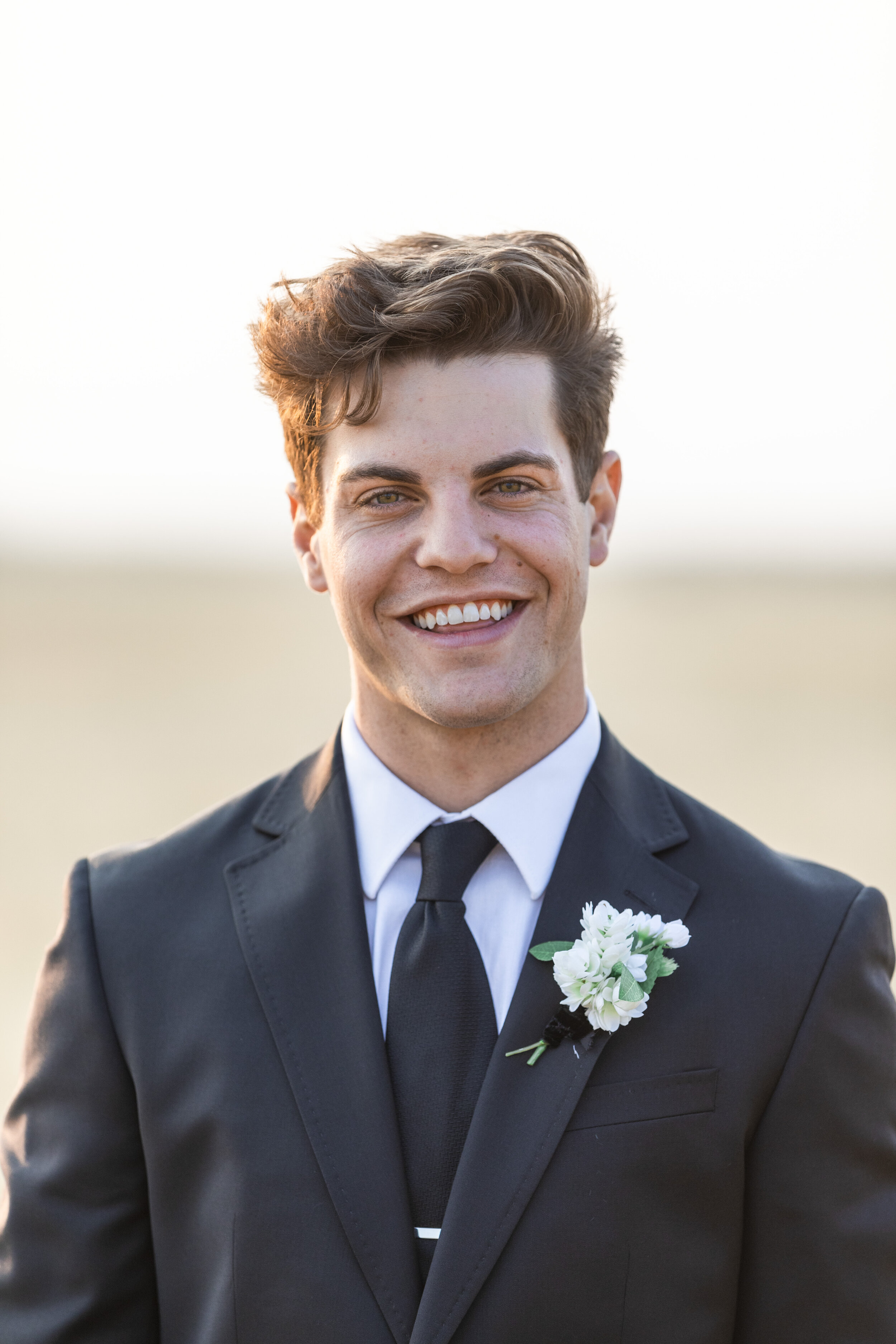  During sunset at Tunnel Springs, Savanna Richardson Photography captures golden sunlight behind the smiling groom wearing a white floral boutonniere. handsome groom groom goals groom in black suit classic wedding colors #savannarichardsonphotography