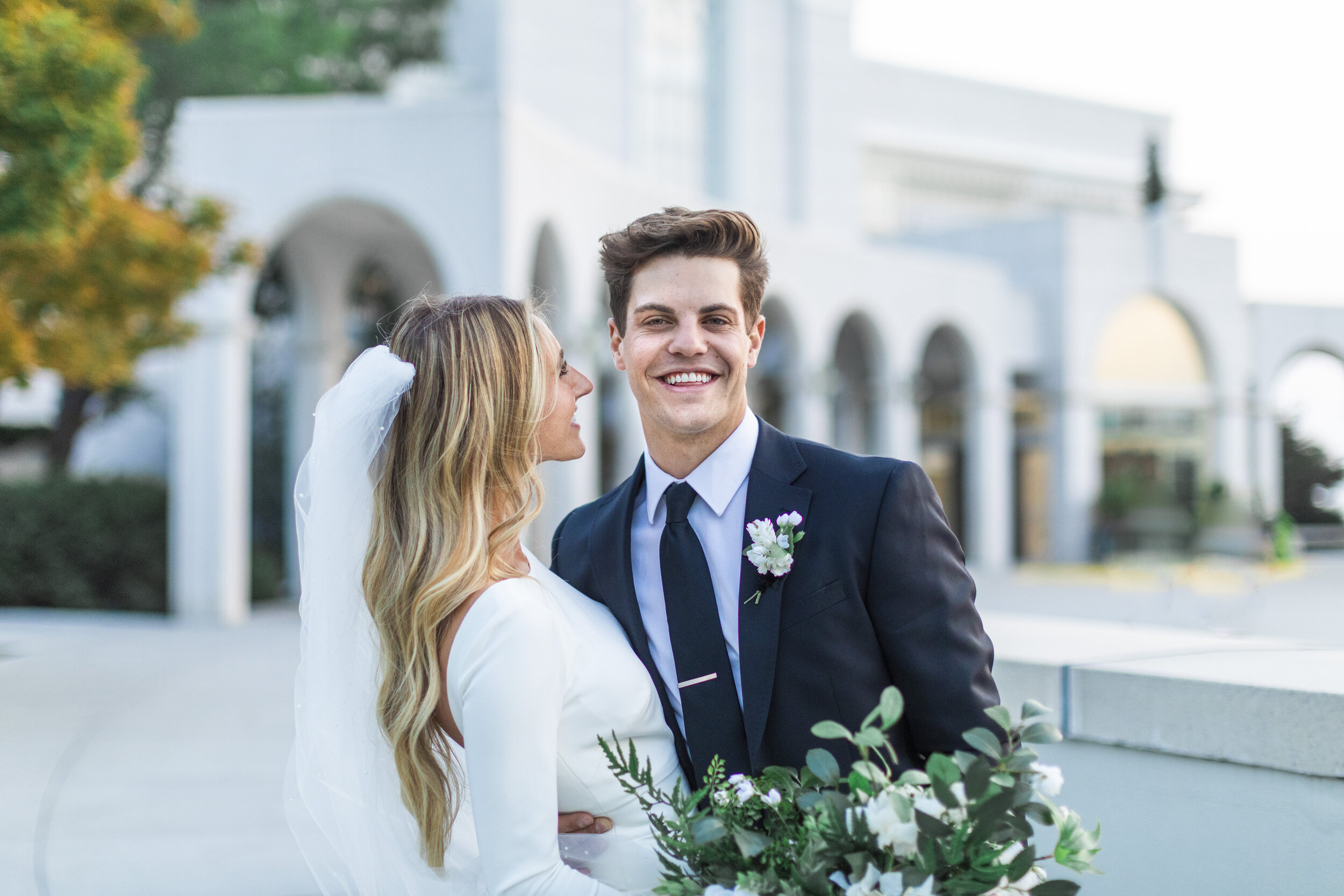  Savanna Richardson Photography captures a bride looking at the groom and smiling as he looks forward in front of the Bountiful Utah Latter-Day Saint Temple. bride and groom temple pictures groom goals dreamy groom dreamy wedding couple #savannaricha