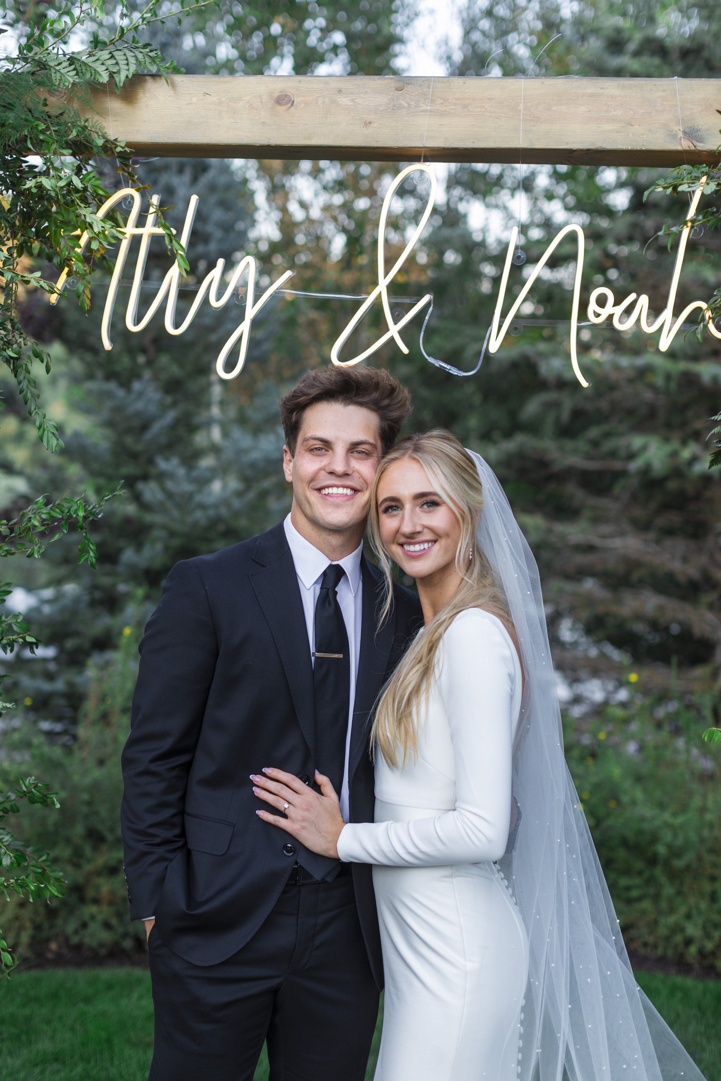  At a wedding reception a newly married couple stand underneath a darling lighted name sign in Northern Utah by Savanna Richardson Photography. lighted sign at reception reception decor ideas unique reception #savannaricharsonphotography #savannarich