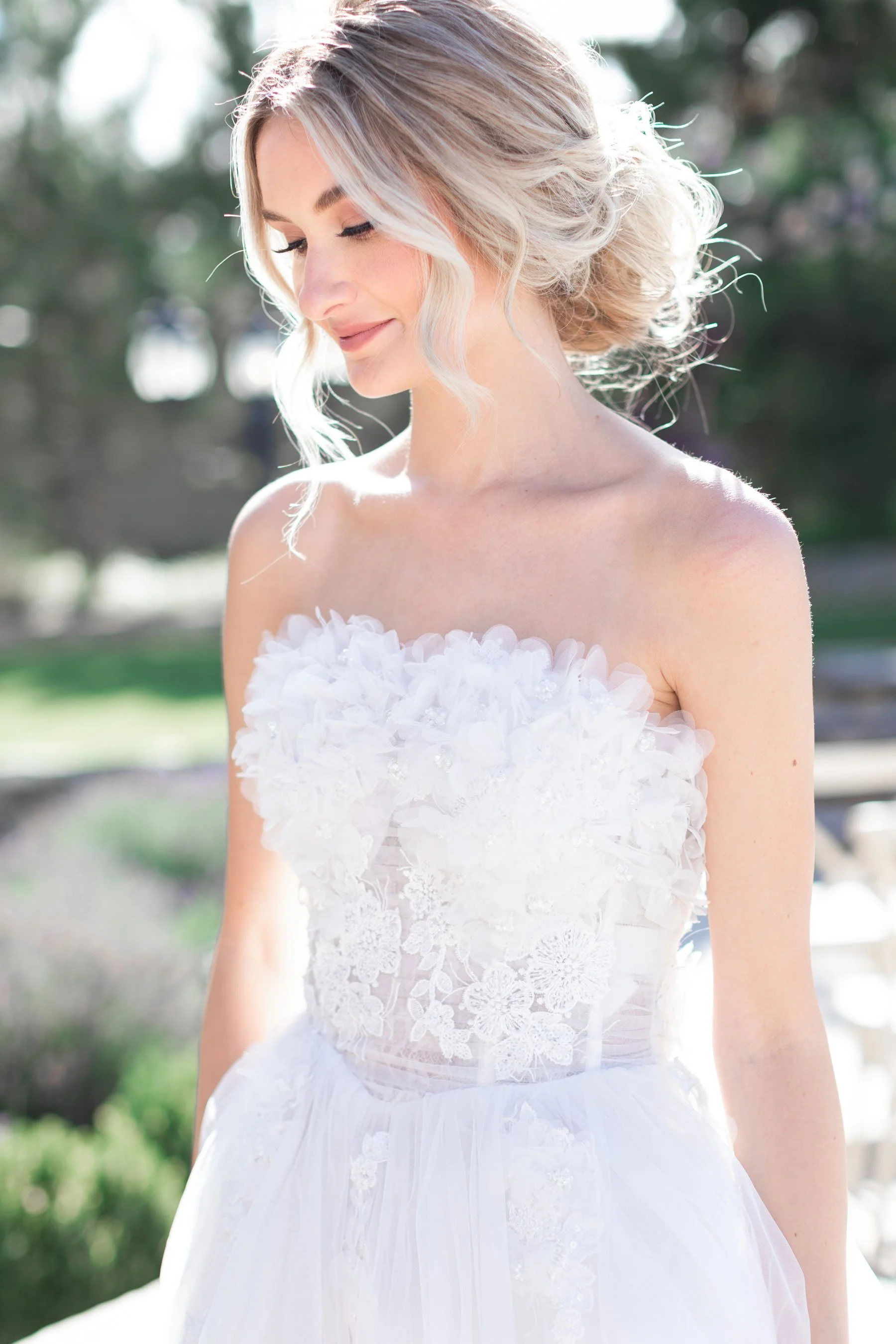  A bride wearing a lace sleeveless wedding dress with a tulle skirt and curled hair updo smiles while looking down by Savanna Richardson Photography in Utah. Bridal photography tips how to look good during bridals #savannarichardsonphotography #Savan