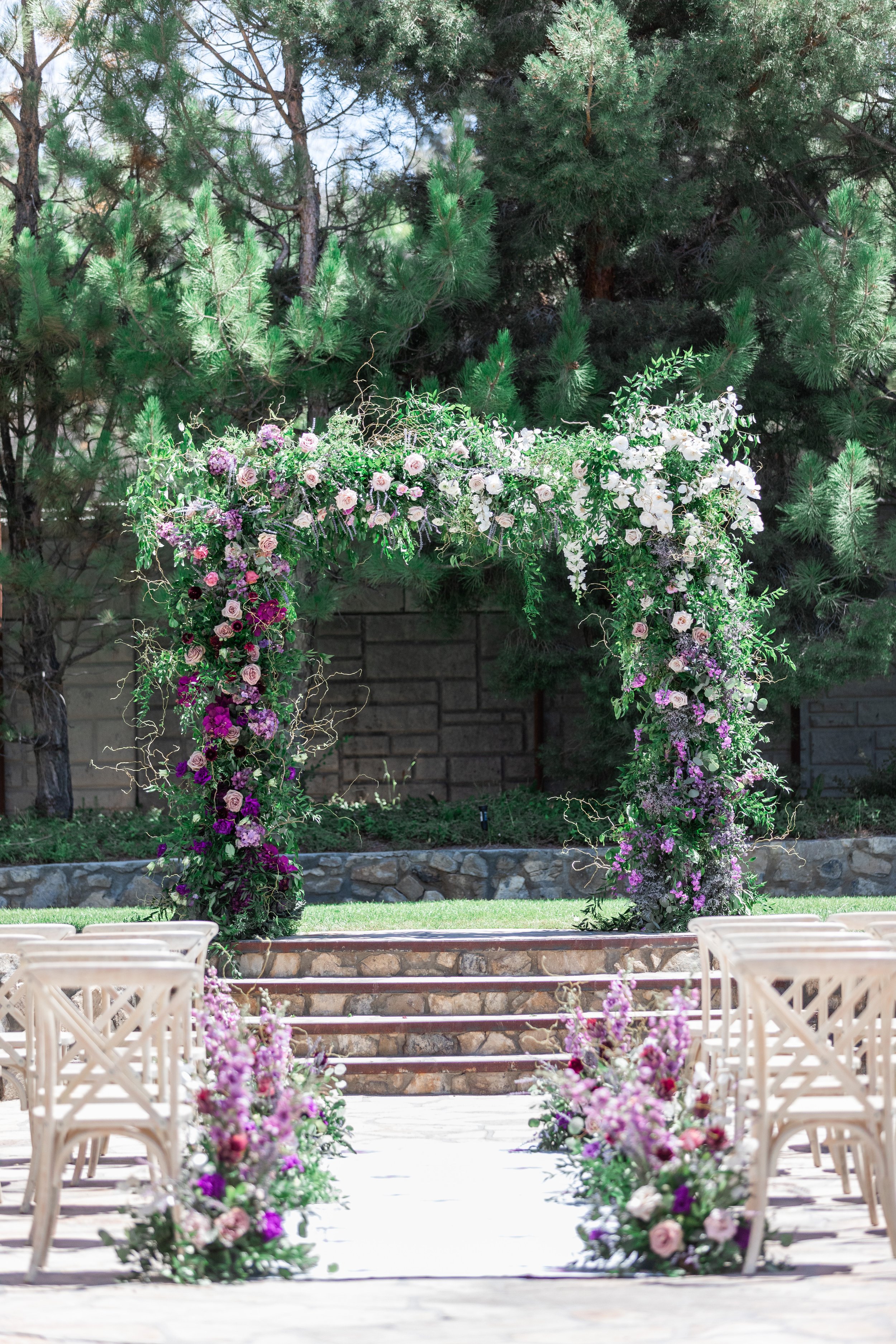  An outdoor wedding set up with a purple flower altar and white wooden chairs by Savanna Richardson Photography. purple floral outdoor altar #savannarichardsonphotography #utahvendor #utahweddingphotographer #MilleFleurDesign #Utahweddingdesigns 