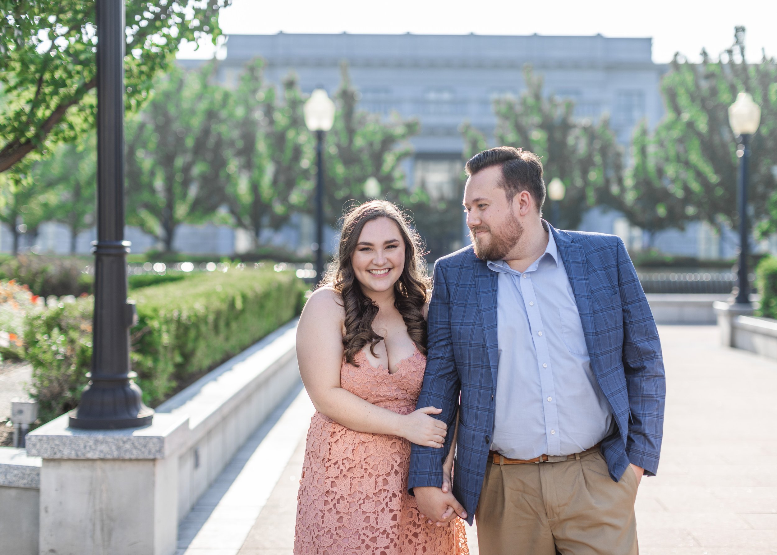  A woman holds a man’s arm wearing a peach dress during a summer engagement session by Savanna Richardson Photography. summer dress engagement outfit #savannarichardsonphotography #Utahcapitolphotography #utahengagements #utahengagementphotographer 