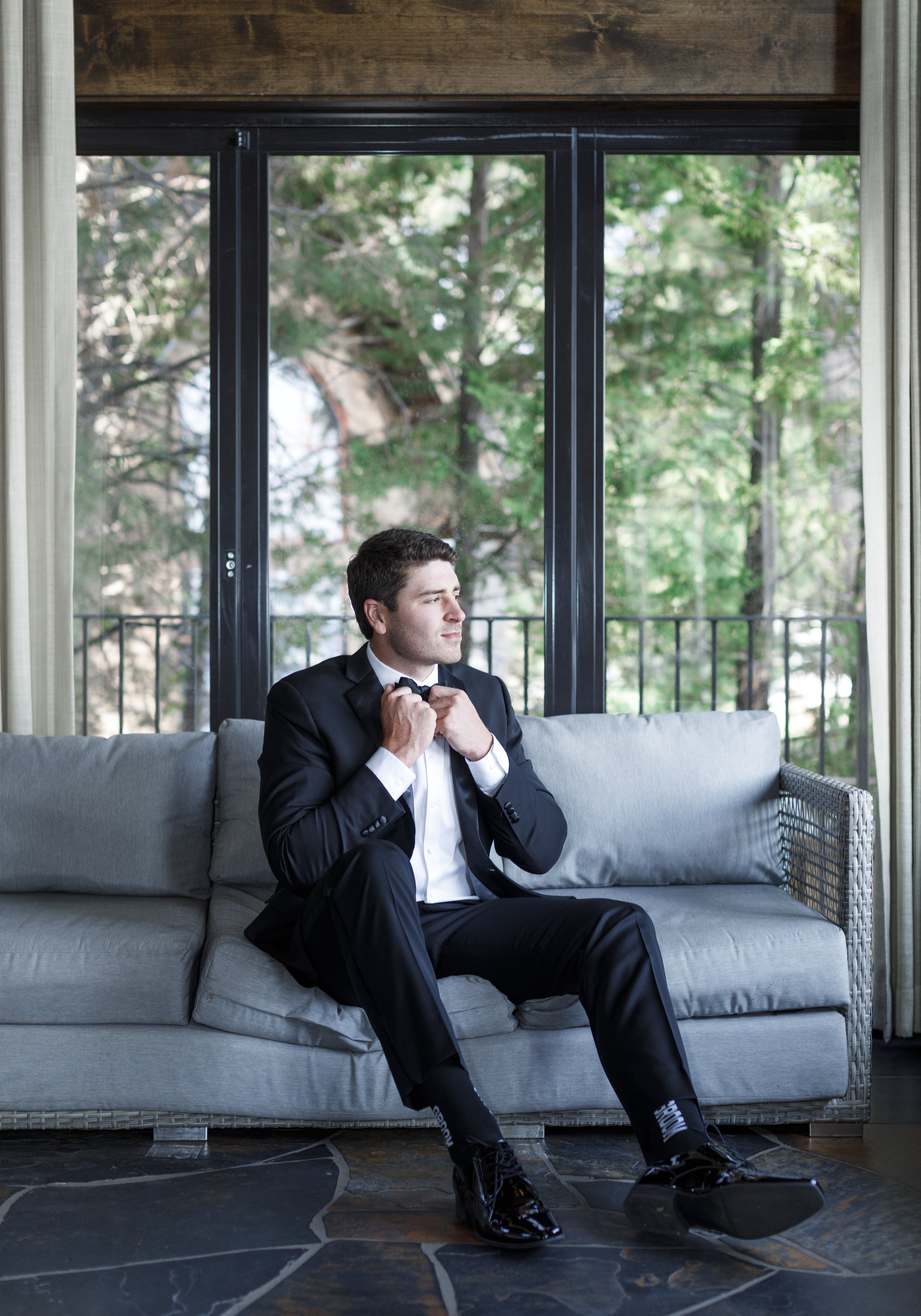  Groom on a couch tying his bowtie in Tahoe captured by Savanna Richardson Photography. Lake Tahoe wedding ideas groom getting ready black bowtie #savannarichardsonphotography #tahoewedding #lakesidewedding #outdoorwedding #summerwedding #laketahoe 