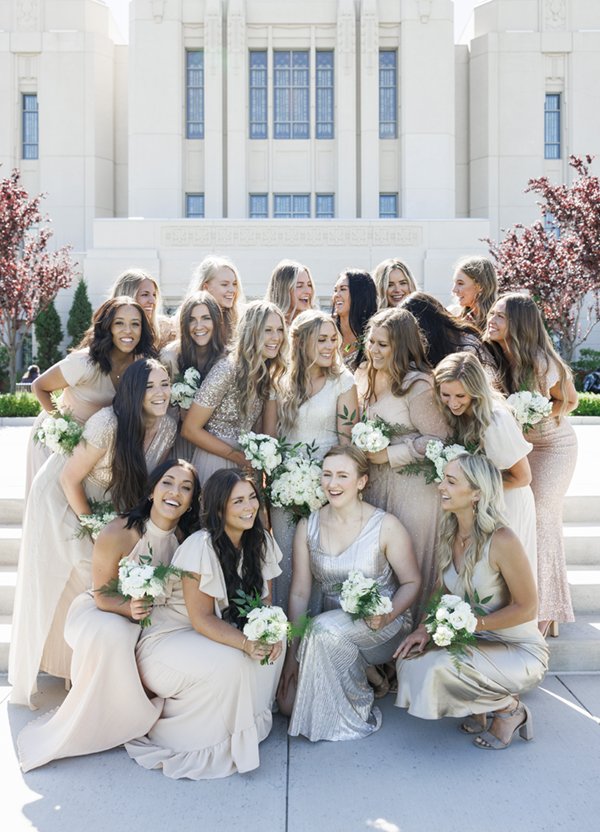  Bride surrounded by twenty bridesmaids wearing blush, cream, and silver sparkl.y bridesmaid dresses. #savannarichardsonphotography #cachevalleyweddingphotographer #weddingposeinspo #bridesmaids #ldstemplewedding #meridianidaho #sparklyweddingparty 