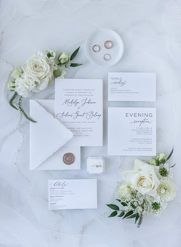  Detail shot of a modern black and white wedding invitation suite on a marble surface next to the wedding bands and cream roses. #weddingdetails #invitationsuite #weddingstationary #weddingringinspo #hisandhersrings #weddingbands #modernweddinginvite