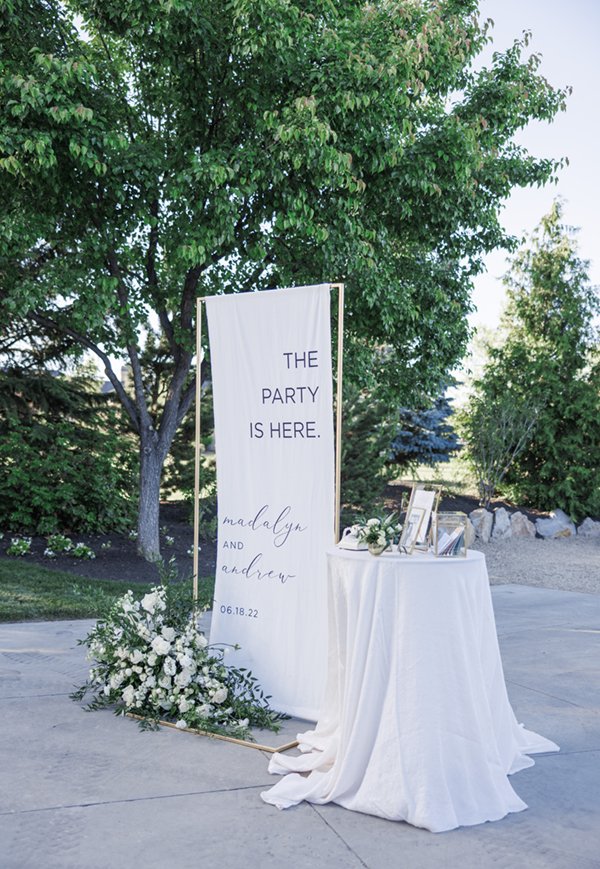  Large welcome sign next to a guest book table and a floral arrangement at the entrance to an outdoor wedding reception. #outdoorwedding #weddingreceptioninspiration #weddingflorals #weddingsigns #decorinspo #cachevalley #tonyinspo #summerwedding 