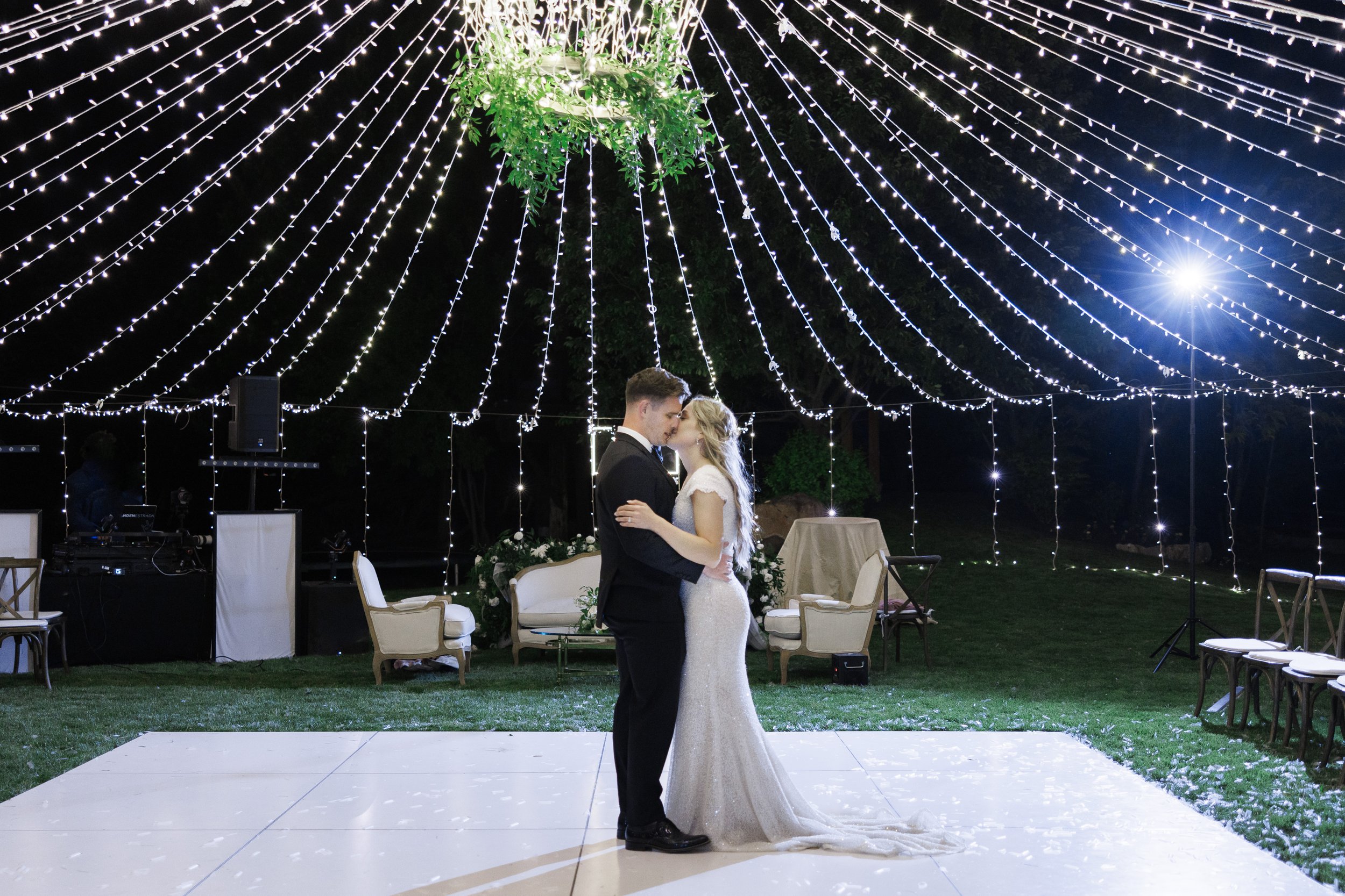  Husband and wife kissing on the dance floor under the canopy of white lights at Tony Grove in Cache Valley. #outdoorweddingreception #kissingposes #newlyweds #weddingdancefloor #receptiondecorationinspo #savannarichardsonphotography #cachevalley 
