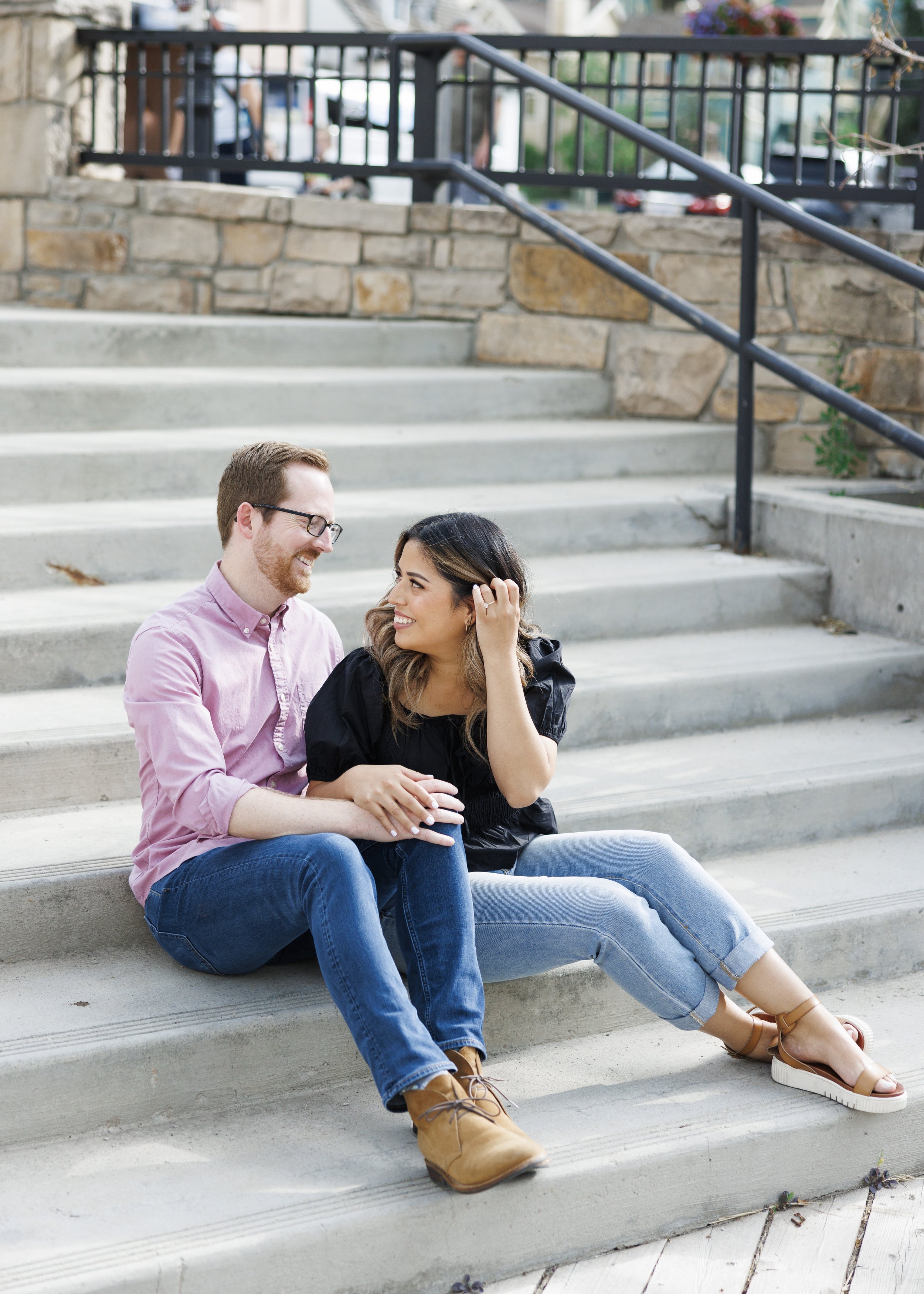  Sitting on city steps a man and woman looking lovingly at one another in Utah summer by Savanna Richardson Photography. pink black jeans #ParkCityEngagements #ParkCityPhotographers #SavannaRichardsonPhotography #SavannaRichardsonEngagements 