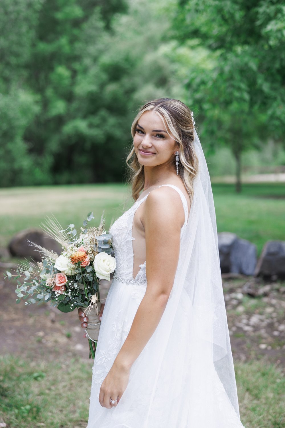  In Mapleton, Utah a bride smiles over her shoulder holding a summer bouquet captured by Savanna Richardson Photography. bridal portrait #SavannaRichardsonPhotography #SavannaRichardsonWeddings #QuietMeadowFarms #MapletonUTweddingphotographers 