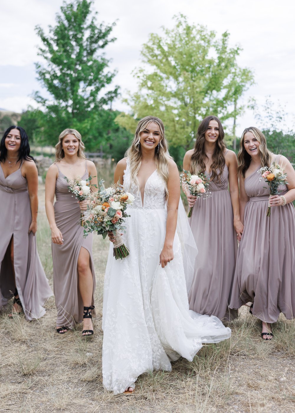  A bride with her bridesmaids wearing muted purple flowy gowns was captured by Savanna Richardson Photography in northern Utah. Northern Utah #SavannaRichardsonPhotography #SavannaRichardsonWeddings #QuietMeadowFarms #MapletonUTweddingphotographers 