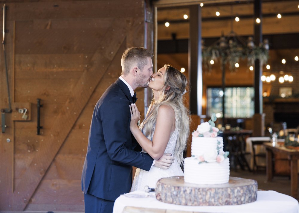  A bride and groom kiss at the cake table on their wedding day by Savanna Richardson Photography. wedding cake 2 tier simple cake #SavannaRichardsonPhotography #SavannaRichardsonWeddings #QuietMeadowFarms #MapletonUTweddingphotographers 