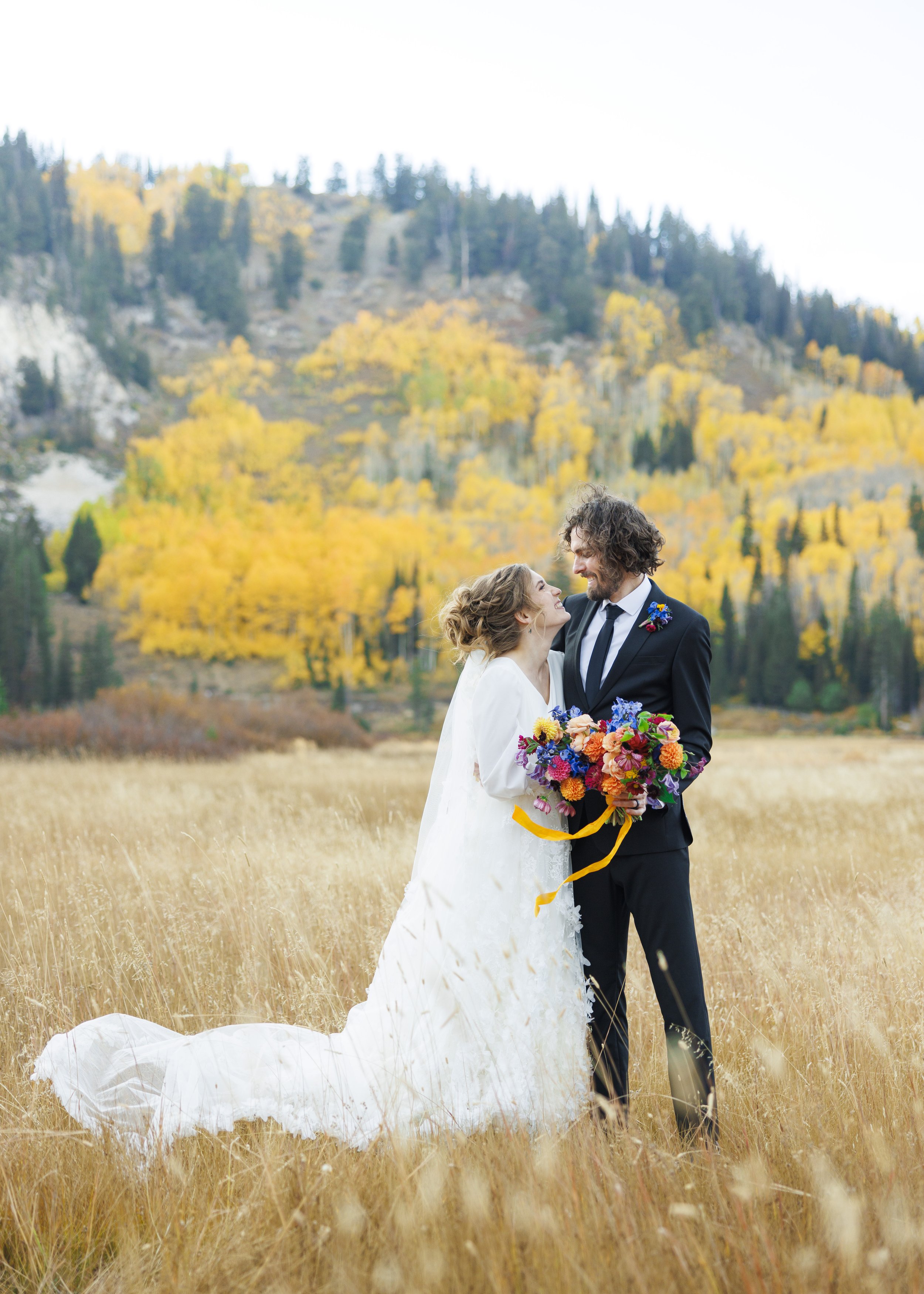  With fall leaves behind them standing in a yellow grass field bride and groom smile by Savanna Richardson Photography. fall UT Wedding #SavannaRichardsonPhotography #SavannaRichardsonFormals #CottonwoodCanyon #WeddingFormals #SLCWedding #fallwed 