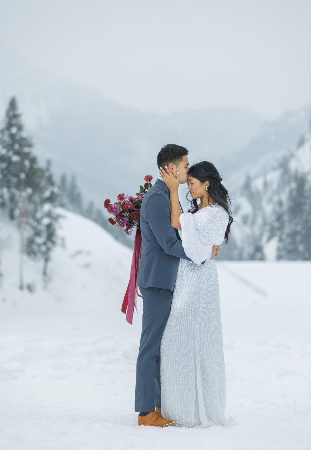 Groom kisses bride on the forehead in snowy mountains of Utah by Savanna Richardson Photography. fog #SavannaRichardsonPhotography #SavannaRichardsonBridals #WinterBridals #WinterWedding #TibbleForkBridals #UtahBridals #MountainBridals 