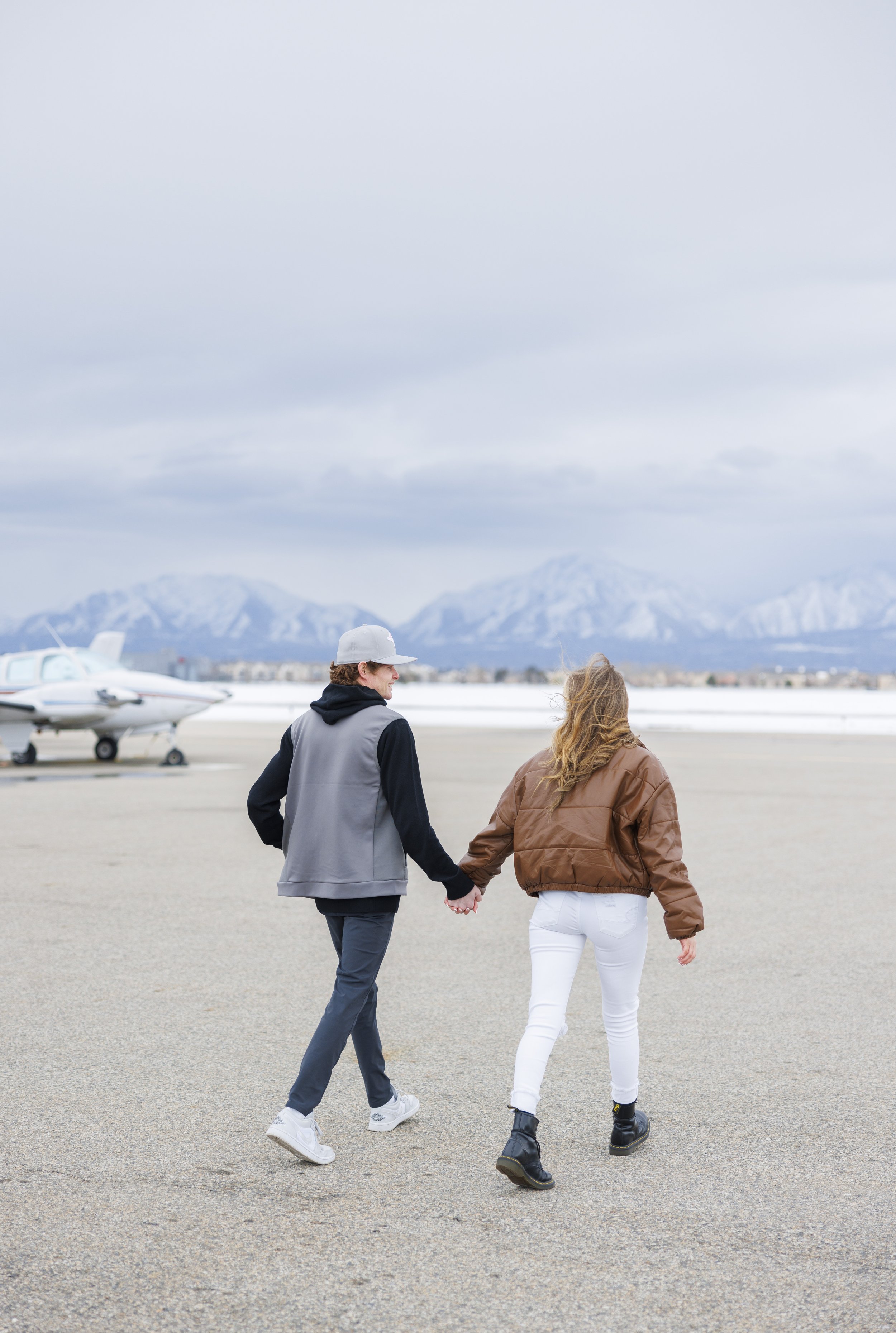  Savanna Richardson Photography captures a boyfriend and girlfriend holding hands through an airport during a proposal. travel proposal landing strip proposal #SavannaRichardsonPhotography #SavannaRichardsonEngagements #utahproposals #helicopterpropo