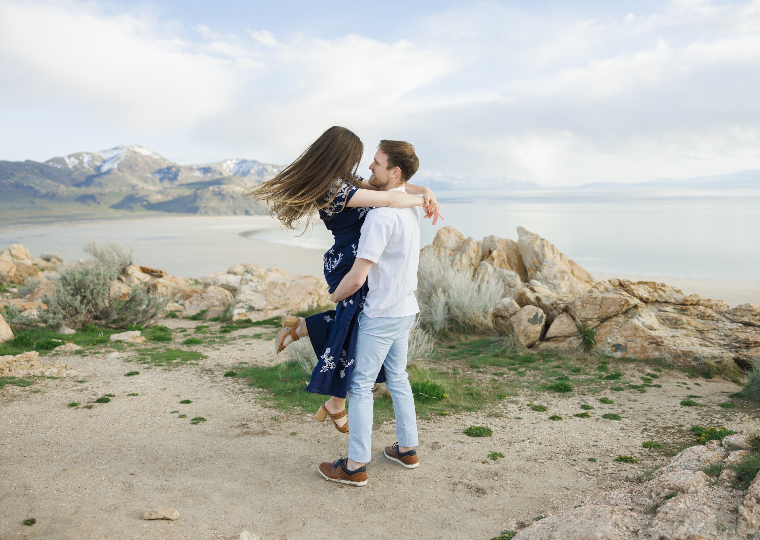  A woman pops her leg up while being picked up by her fiance on the top of Antelope Island by Savanna Richardson Photography. Outdoor engagements breathtaking backdrops #SavannaRichardsonPhotography #SavannaRichardsonEngagements #UtahEngagements #Ant