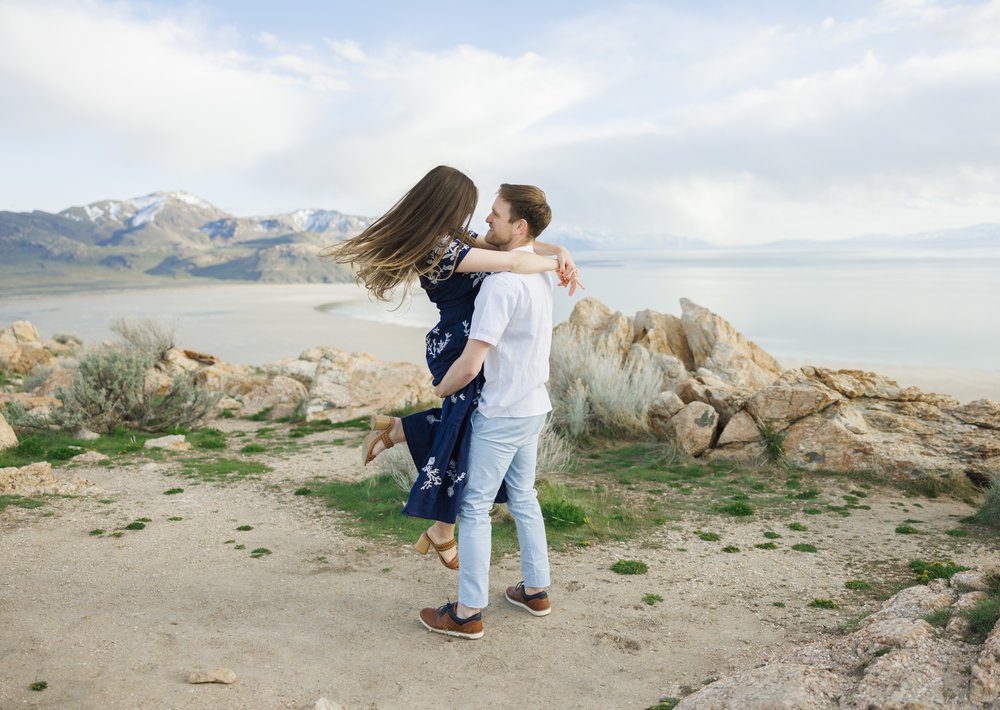  A woman pops her leg up while being picked up by her fiance on the top of Antelope Island by Savanna Richardson Photography. Outdoor engagements breathtaking backdrops #SavannaRichardsonPhotography #SavannaRichardsonEngagements #UtahEngagements #Ant