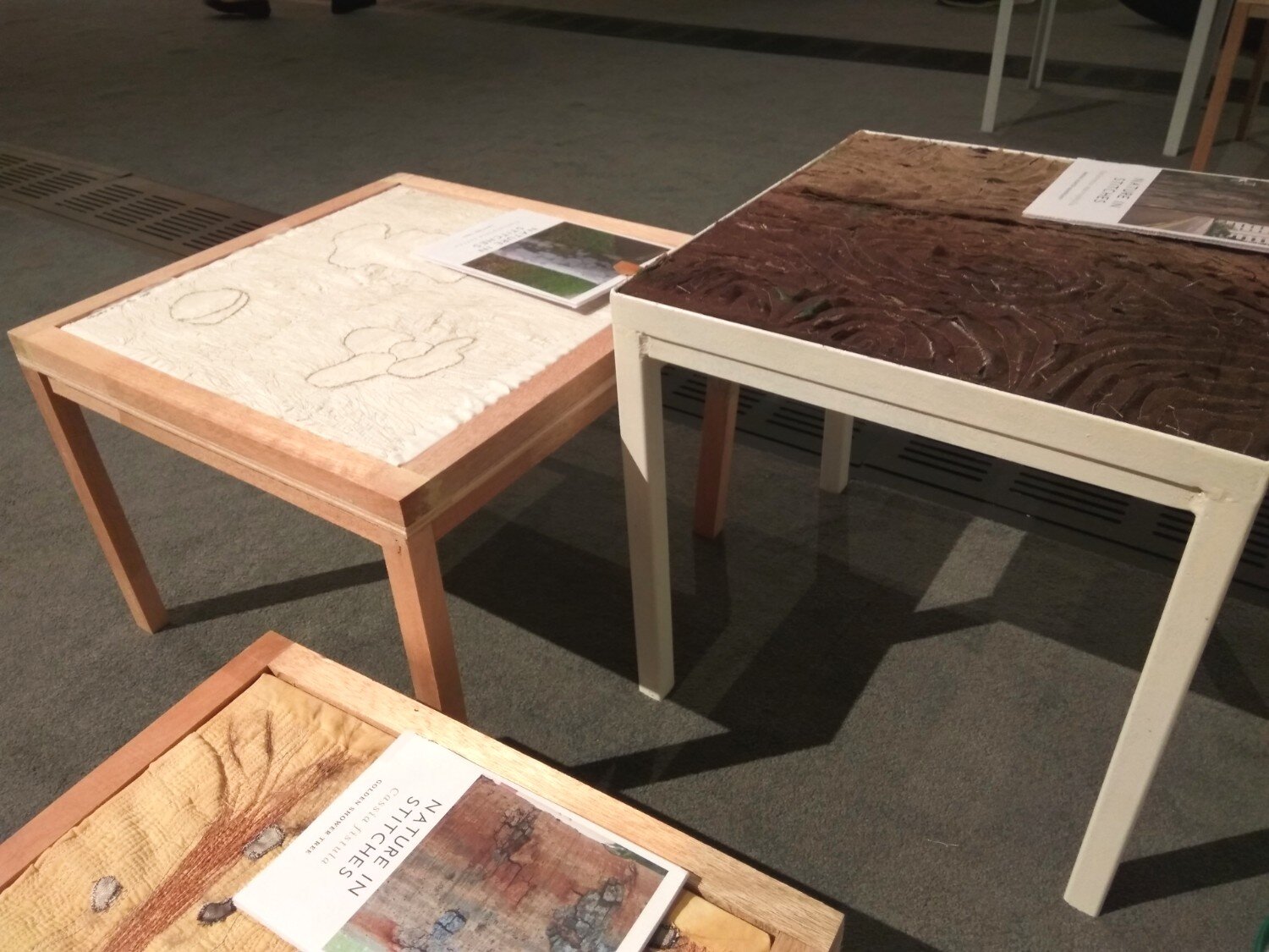 Textile art installation comprising interpretations of tree bark embroidered on coffee tables.