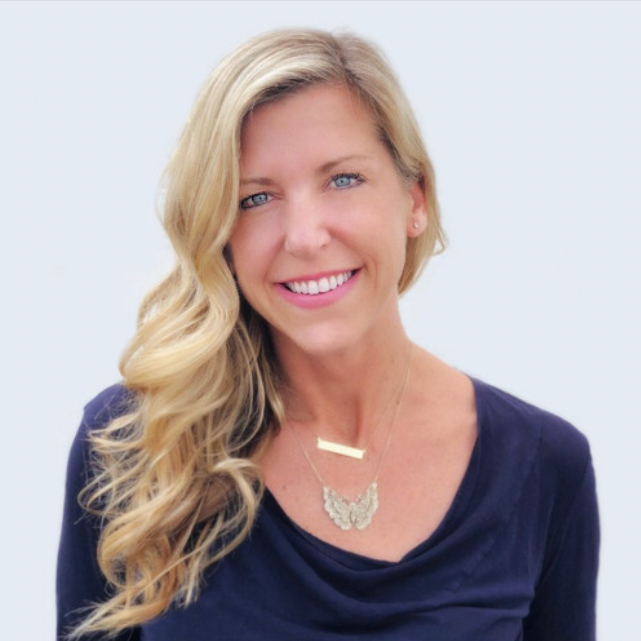 A woman with long blonde hair and blue eyes smiling, wearing a navy blue top and layered necklaces, against a light background.