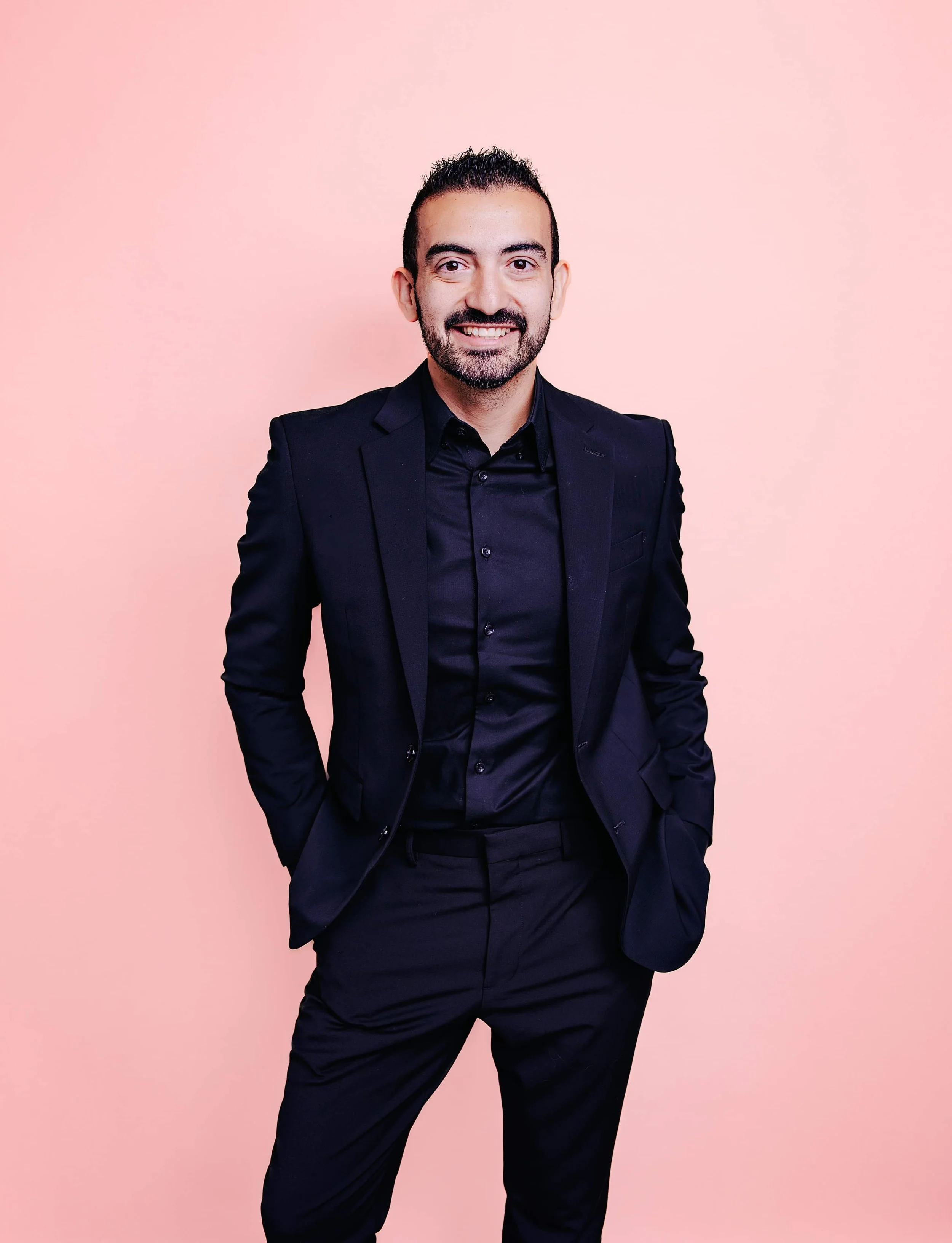 Professional corporate headshot of a man in a dark suit photographed against a soft pink studio backdrop.