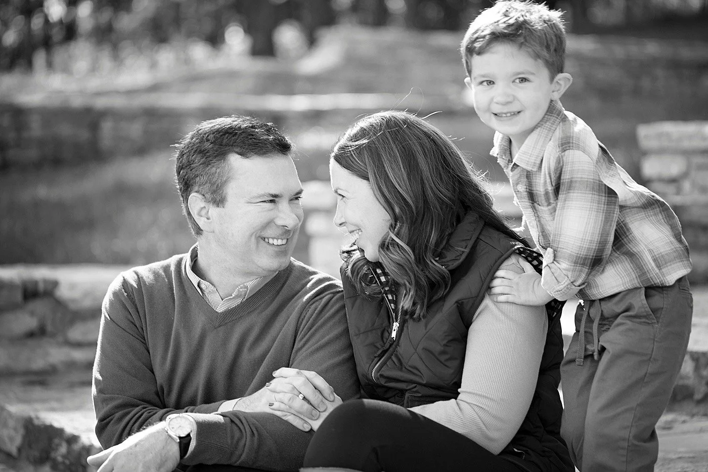 A family of tree, mom and dad looking at each other joyfully, while their kid smiles at the camera. Timeless black and white picture.