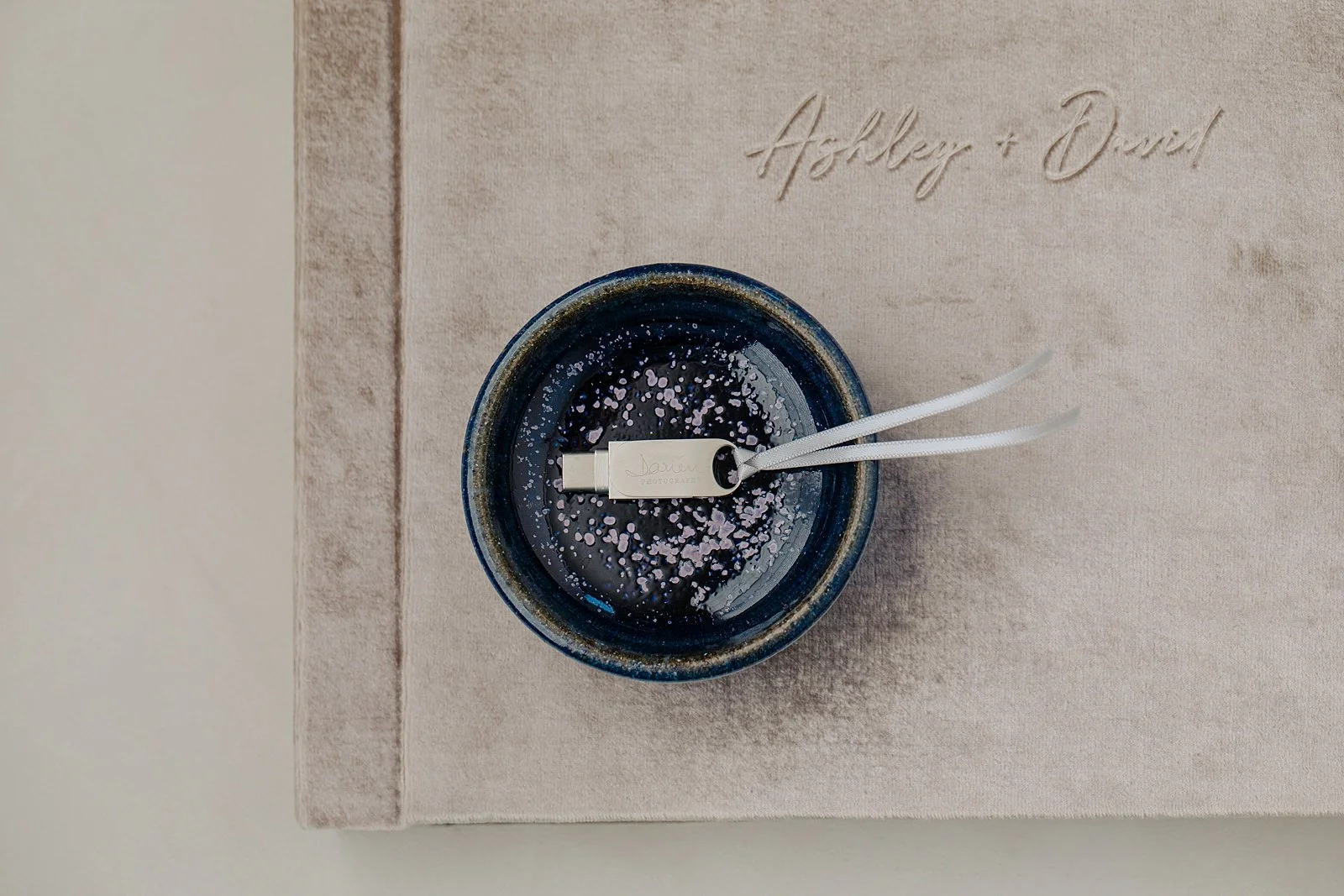 USB flash drive with Darien Photography's logo, on top of a velvet cover wedding album.