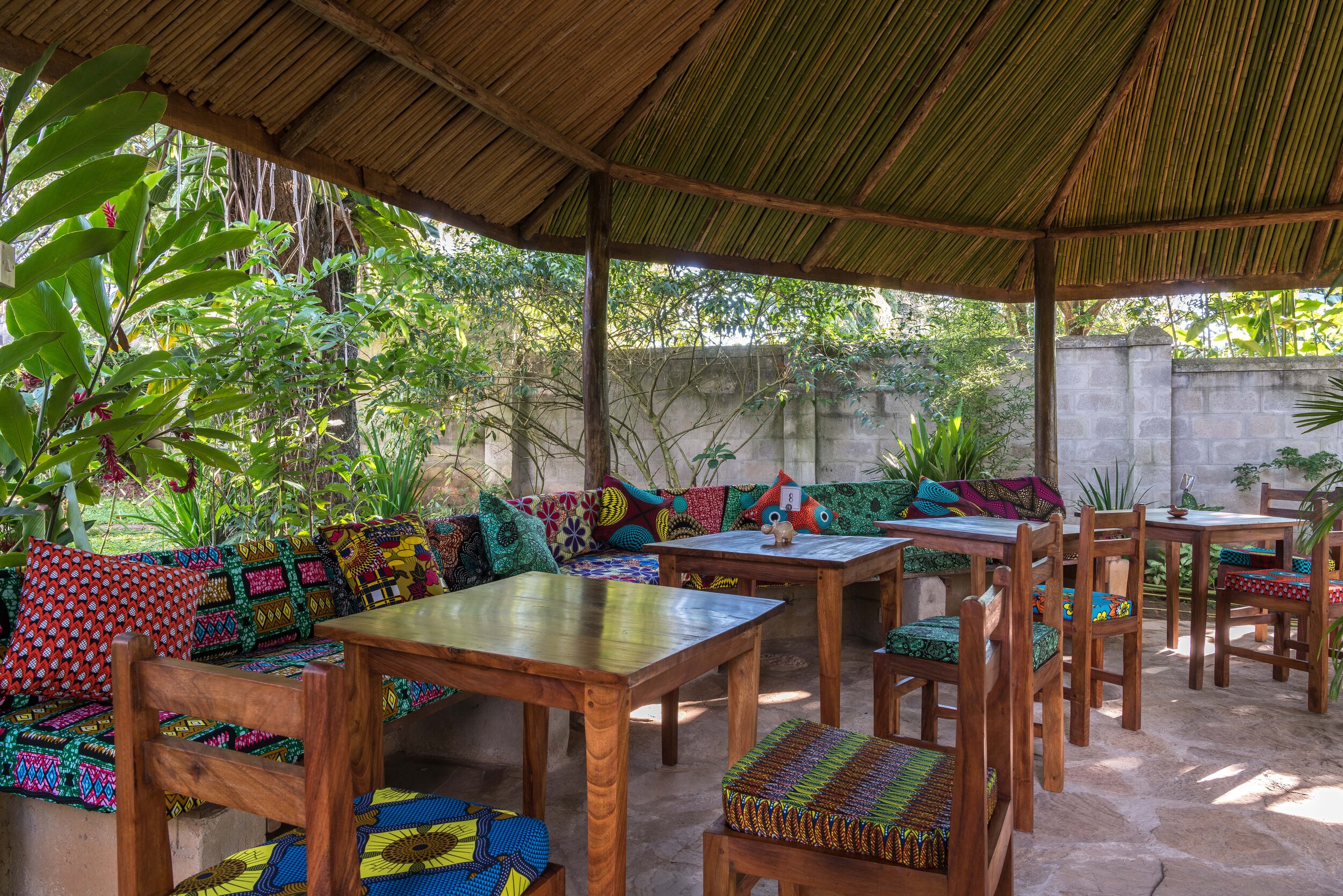 Seated area with colourful kitenge sofa and cushions behind wooden tables