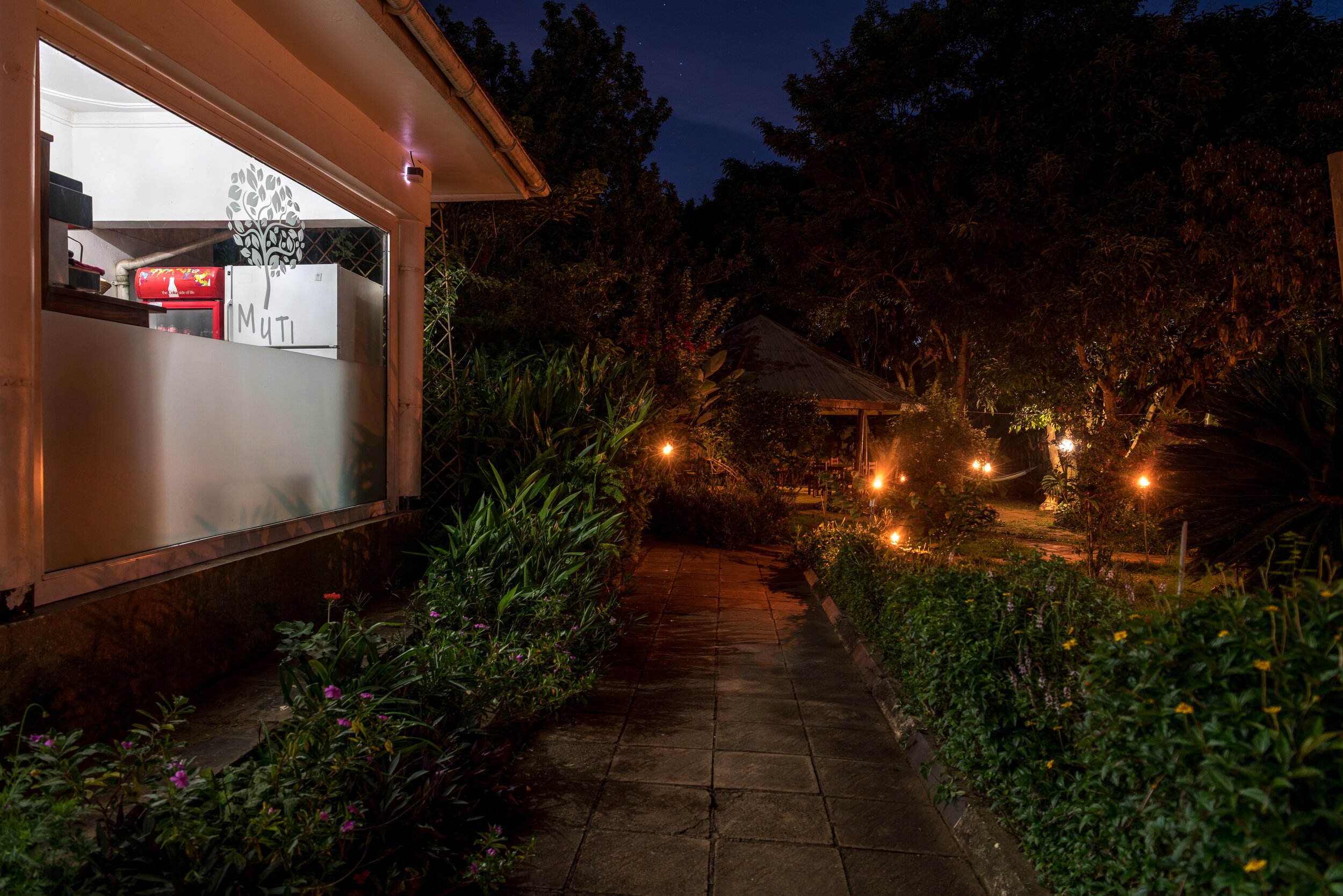 Night shot of Muti logo on frosted glass coffee bar beside garden with lanterns